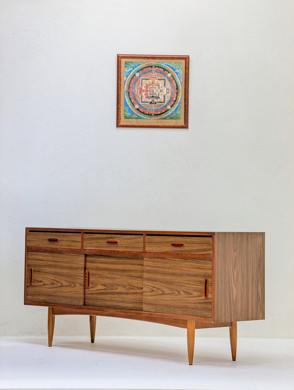 Mid-century modern wooden sideboard with drawers and sliding doors under a framed colorful geometric wall art