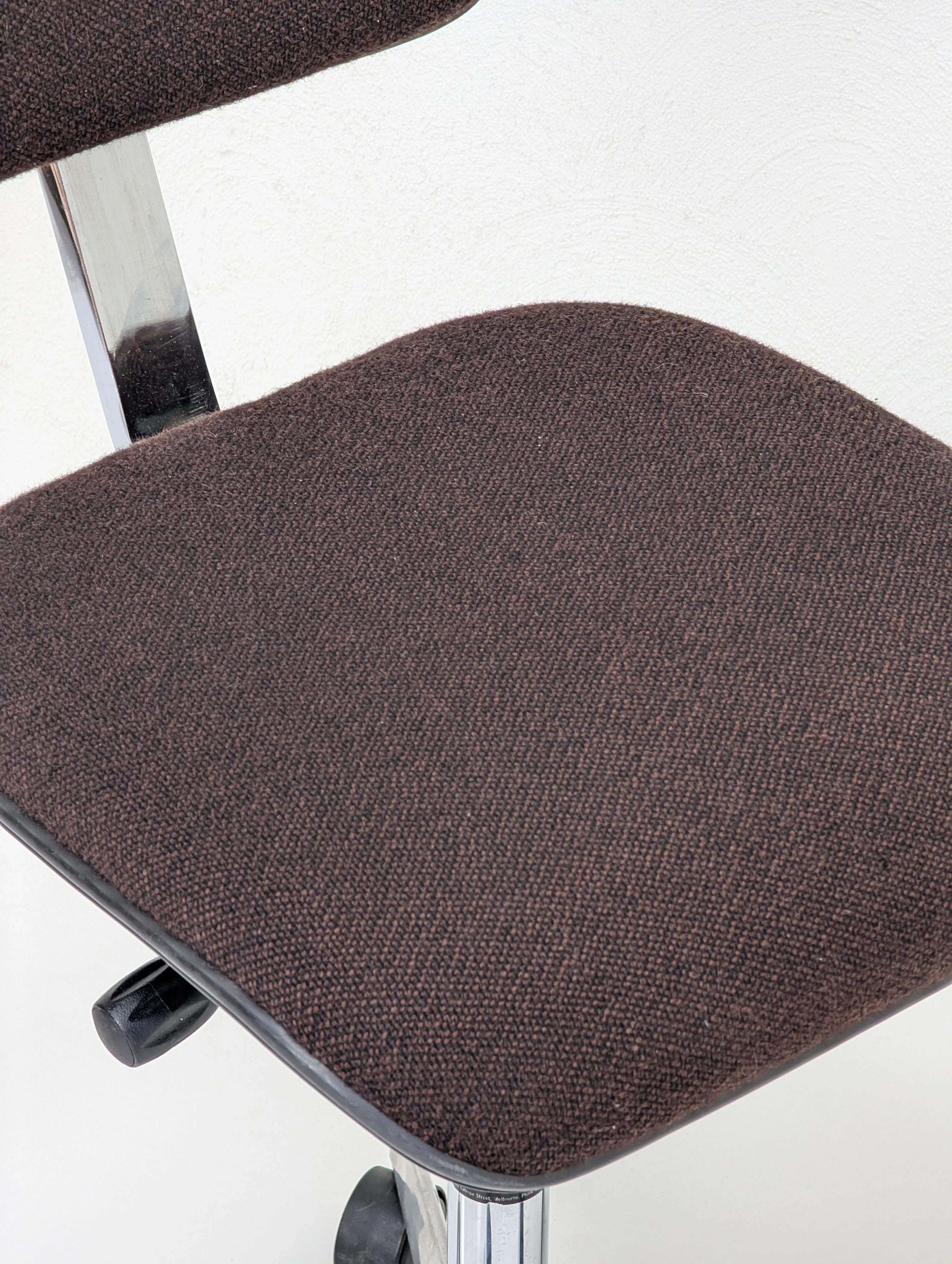 Close-up of brown fabric office chair seat with chrome metal legs and adjustment knob
