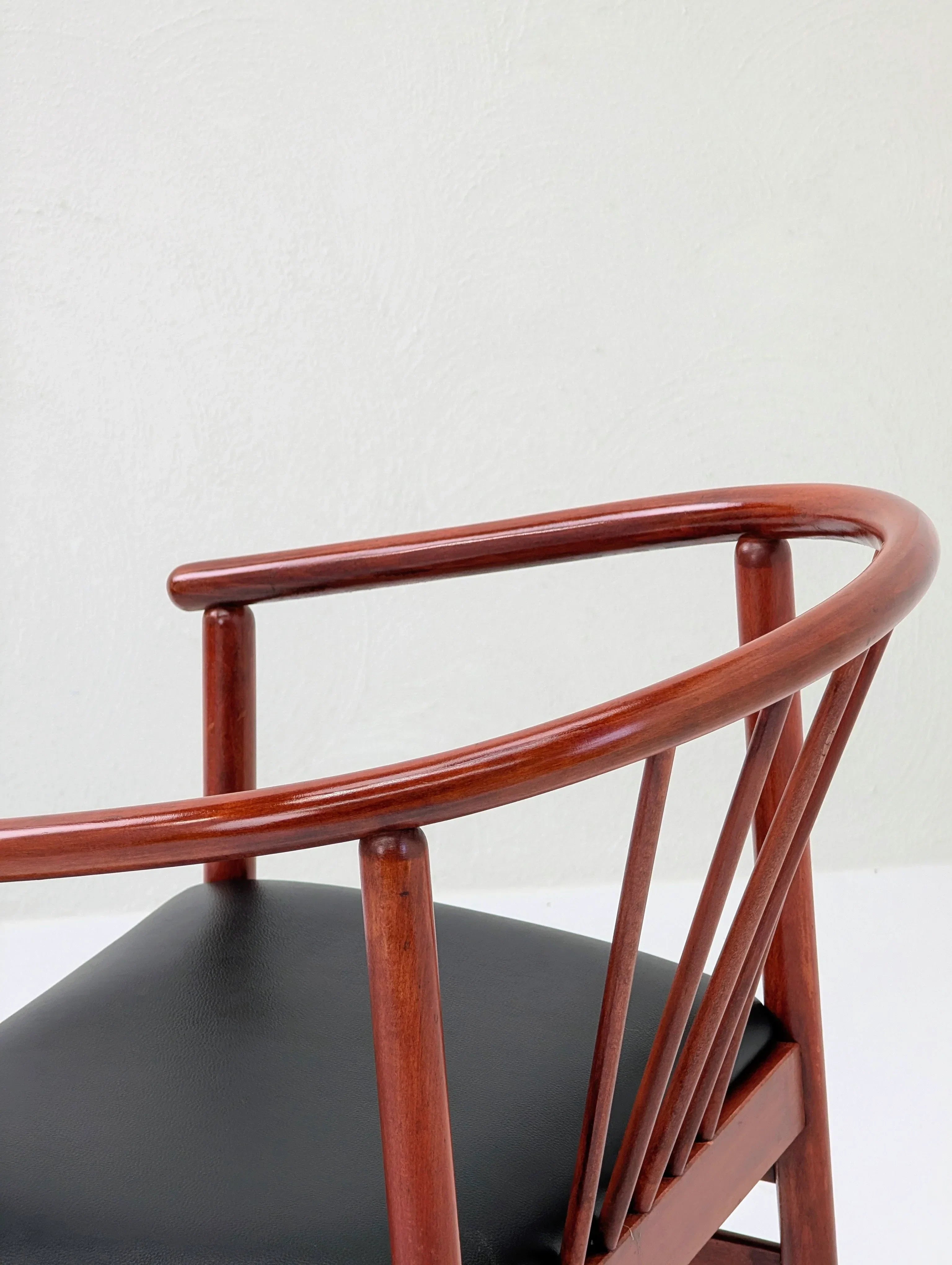 Modern wooden chair with curved backrest and black leather seat against a light wall