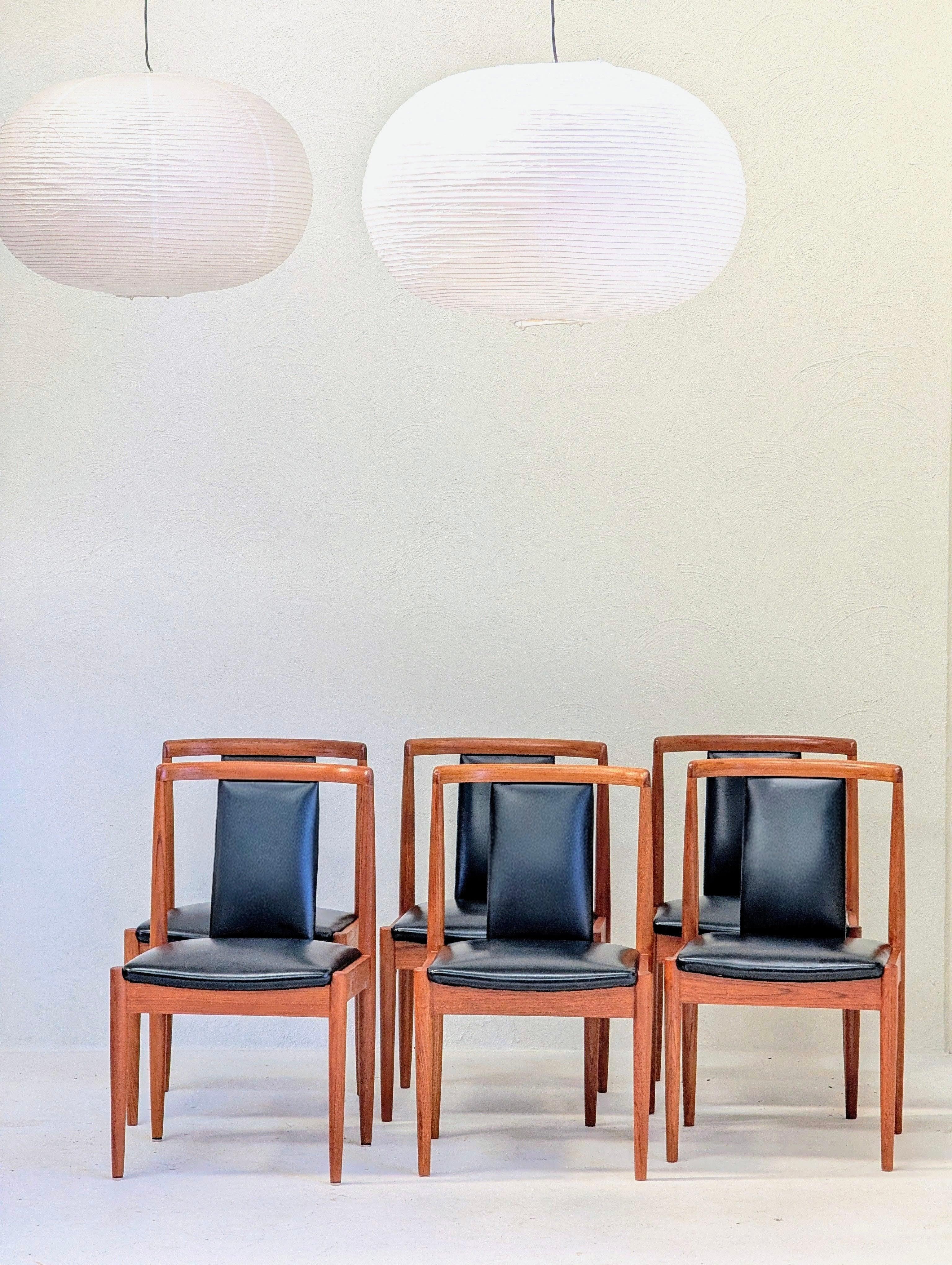 Set of six mid-century modern dining chairs with black leather seats and wooden frames under two white pendant lamps
