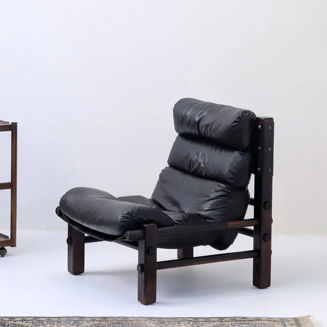 Vintage black leather lounge chair with dark wood frame in minimalist room