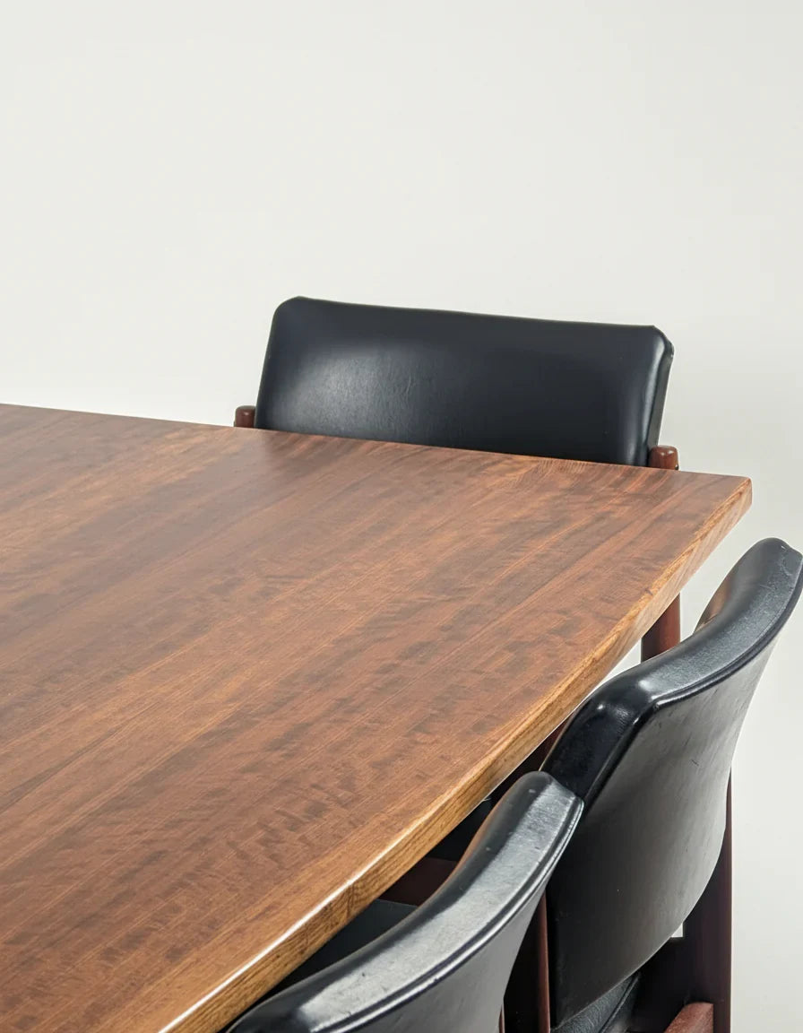 Close-up of wooden dining table corner with three black leather chairs against white wall