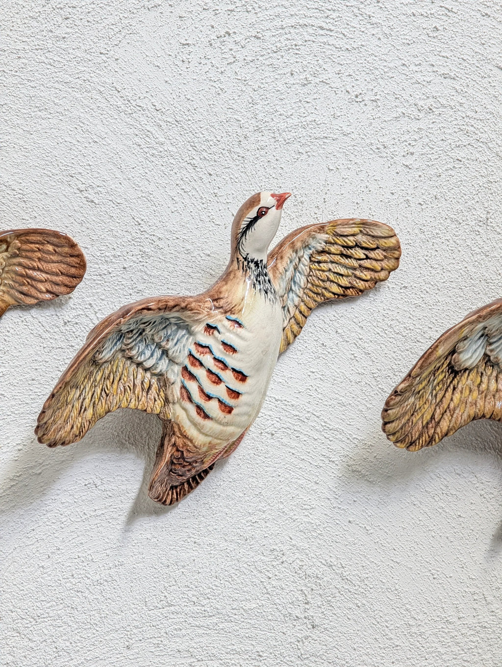 Decorative ceramic bird sculpture with outstretched wings mounted on textured white wall