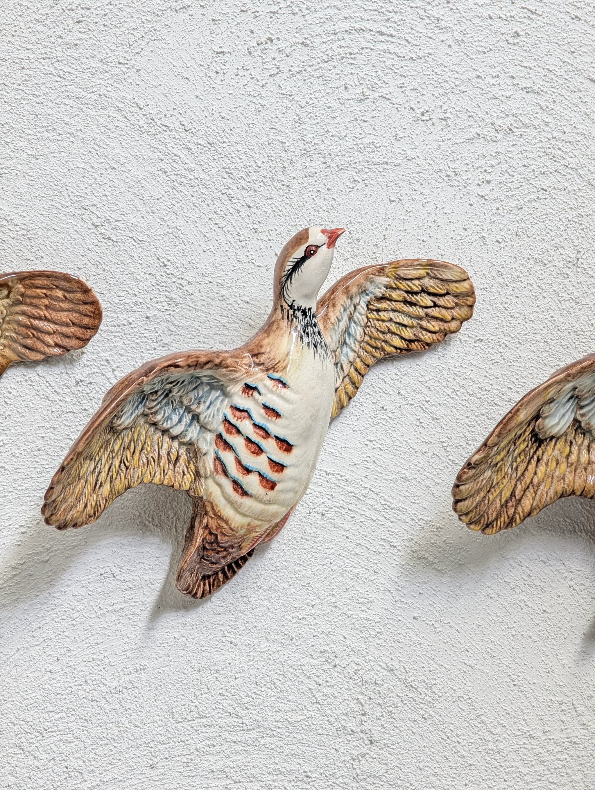 Decorative ceramic bird sculpture with outstretched wings mounted on textured white wall