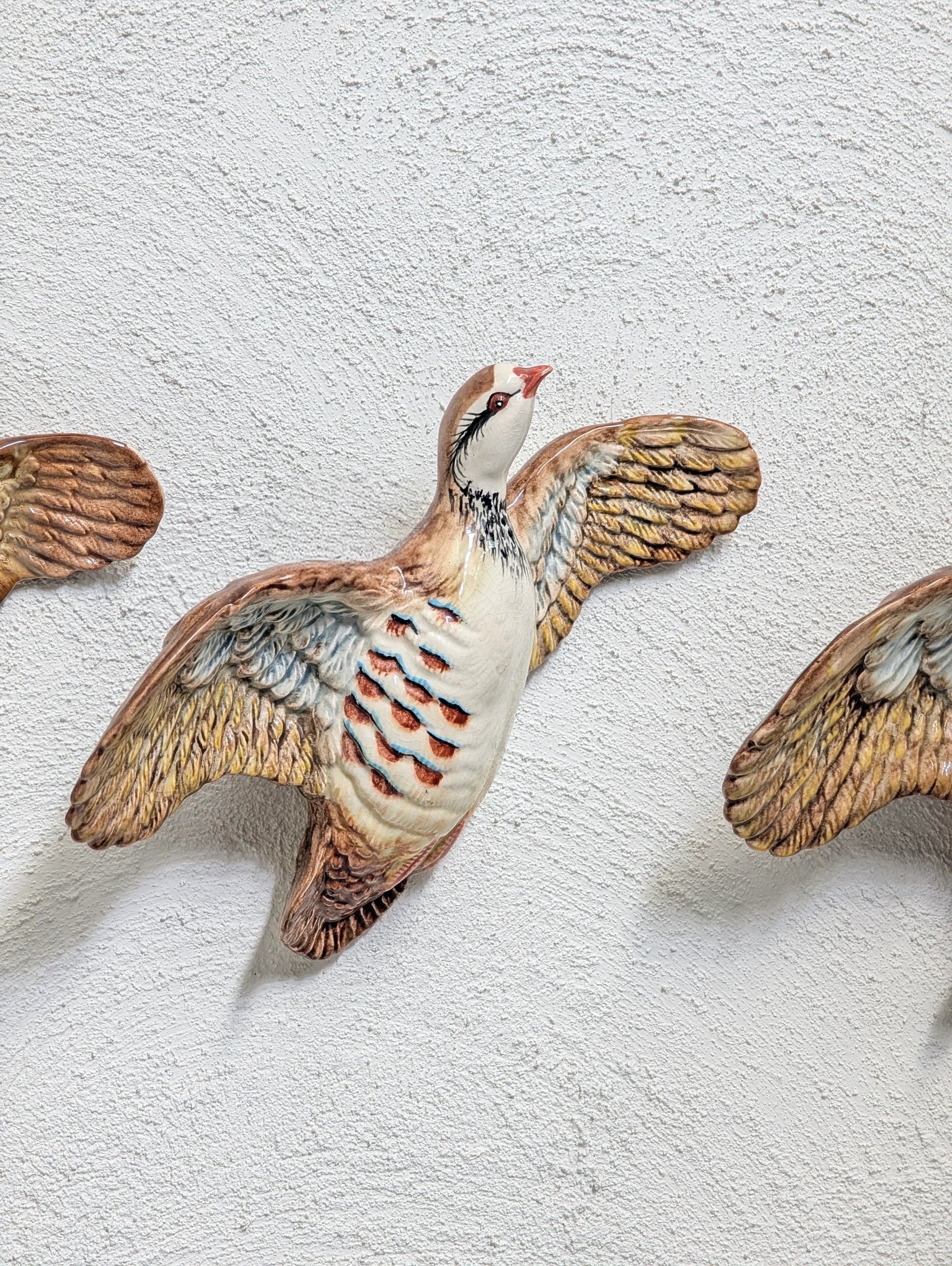 Decorative ceramic bird sculpture with outstretched wings mounted on textured white wall