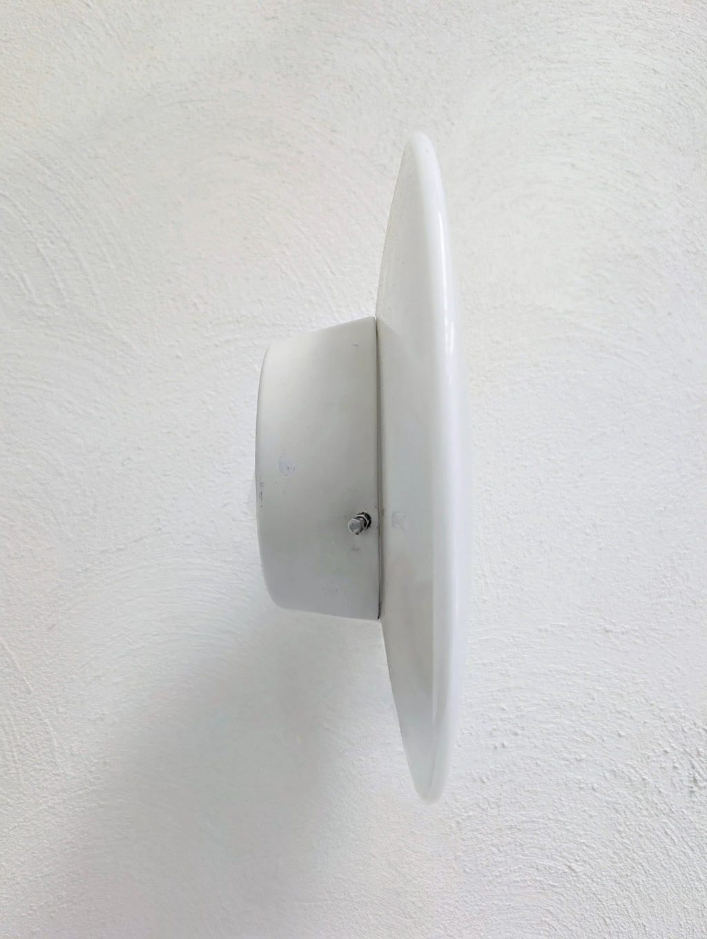 White circular metal wall vent mounted on textured white wall