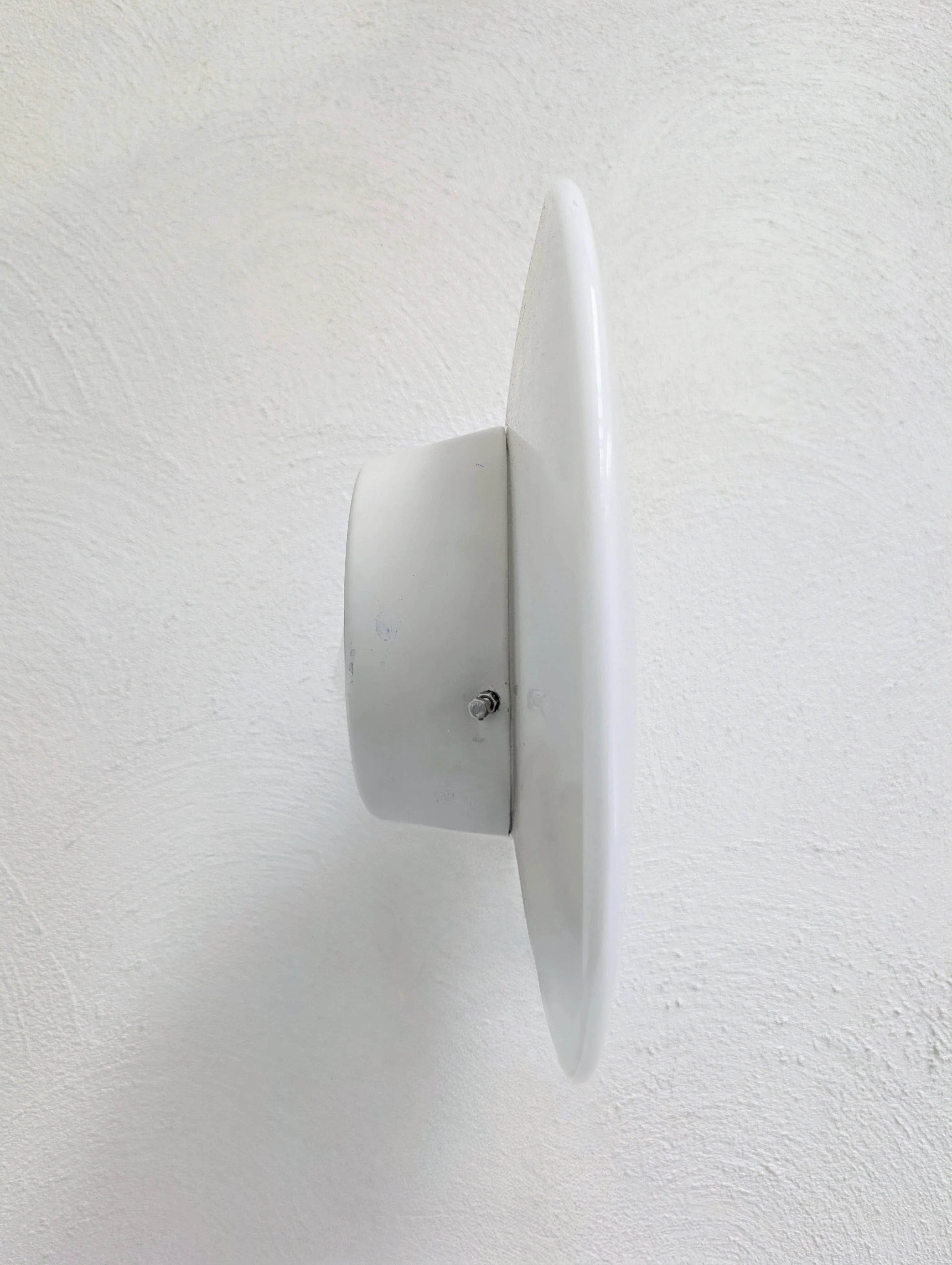 White circular metal wall vent mounted on textured white wall