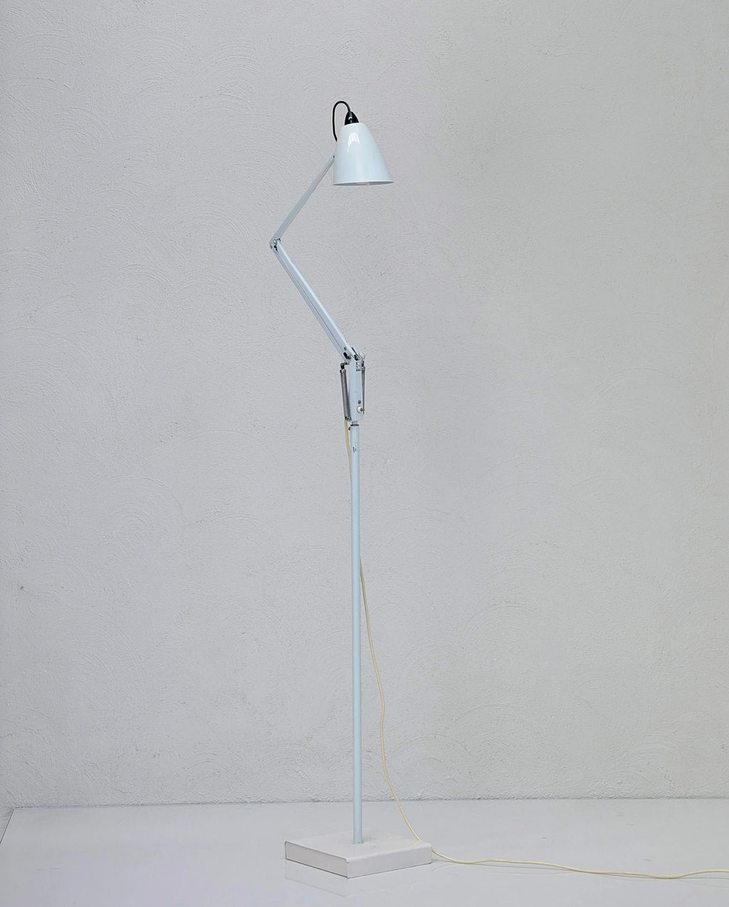 Modern adjustable white metal floor lamp with angled arm against light textured wall