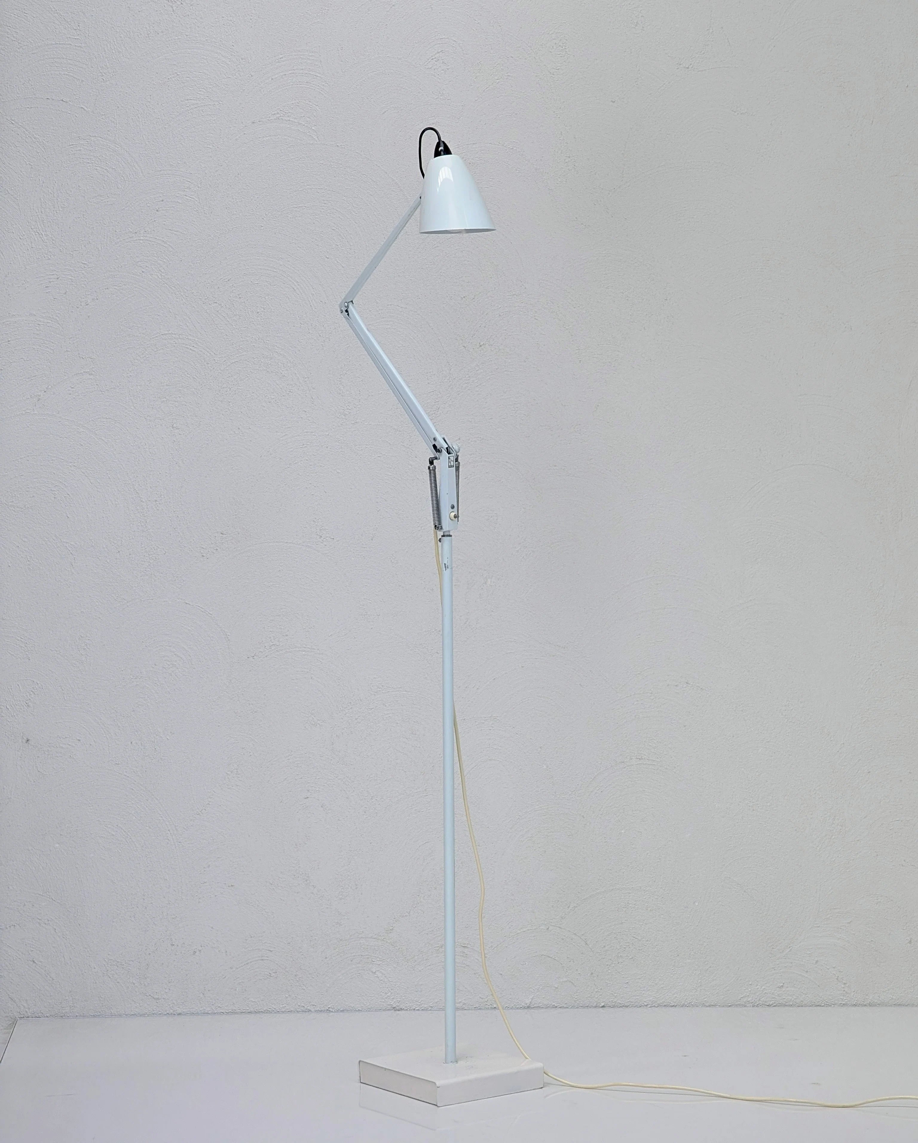 Modern adjustable white metal floor lamp with angled arm against light textured wall
