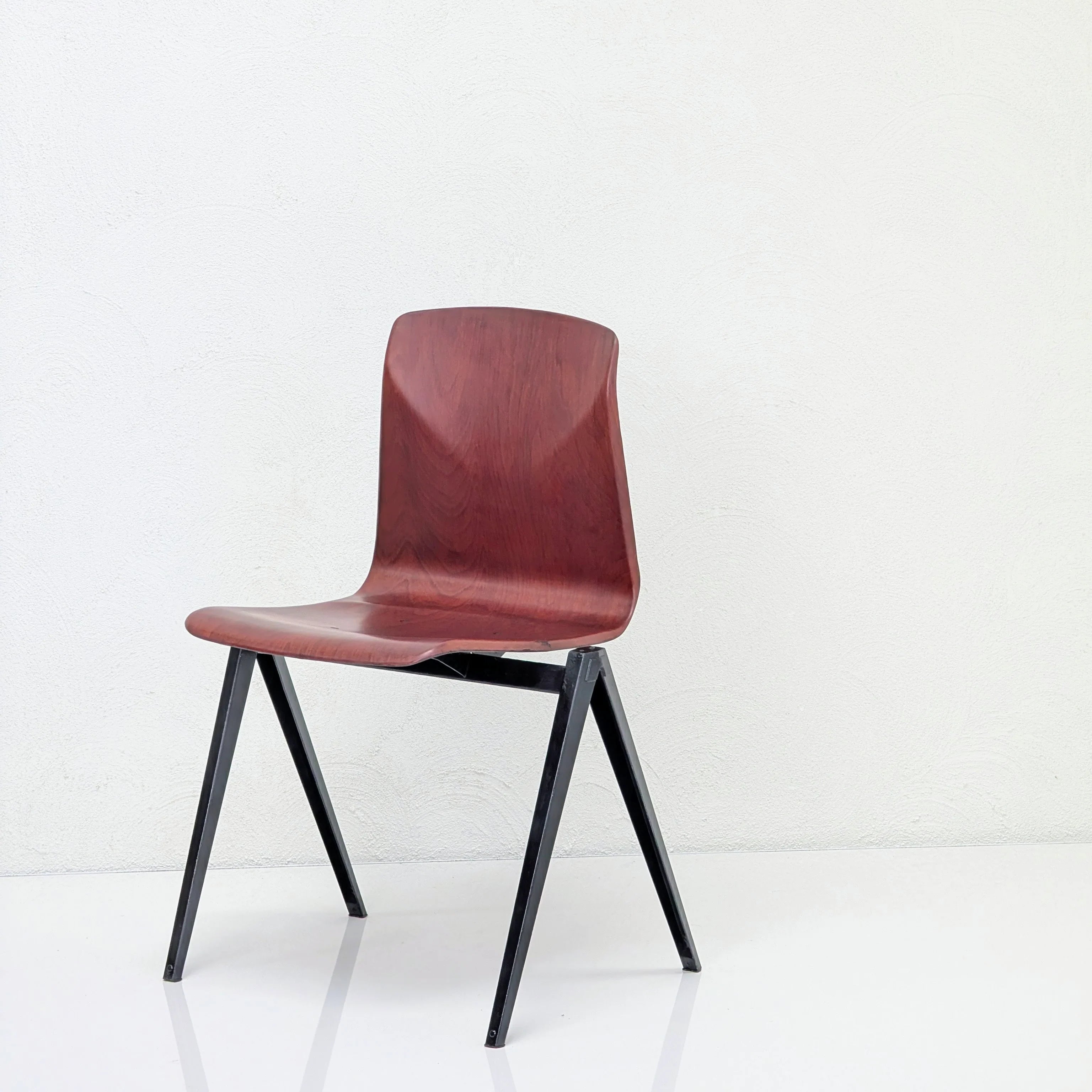 Modern wooden chair with dark metal legs on a white reflective floor against white textured wall