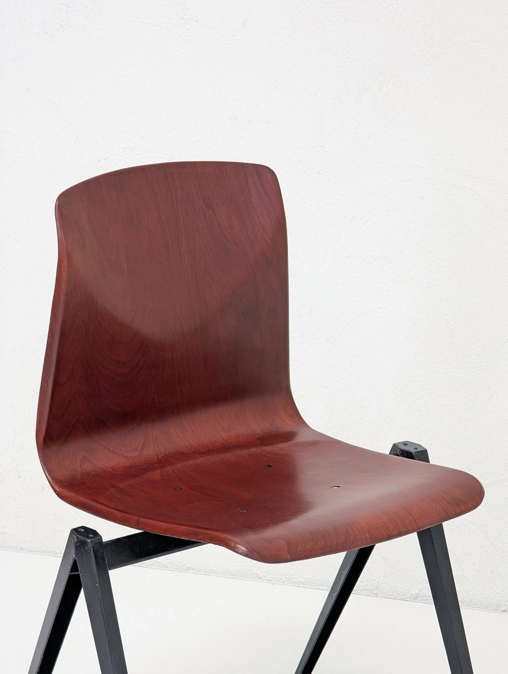 Modern wooden seat with curved back mounted on black metal frame against white wall
