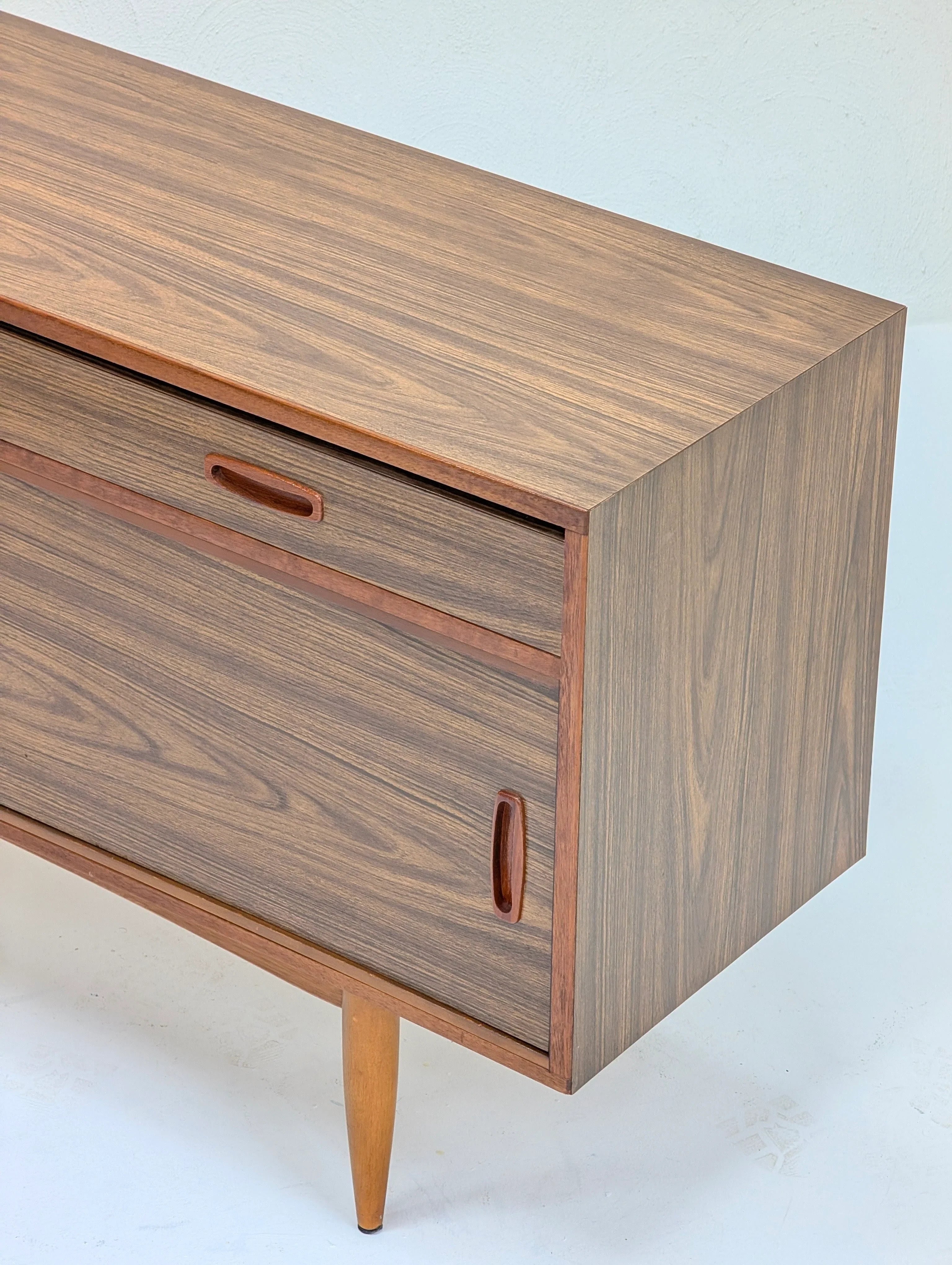Mid-century modern wooden cabinet with tapered legs and integrated handles in natural finish