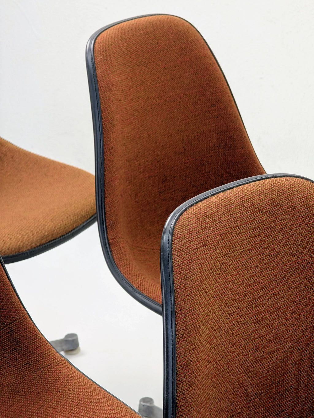Close-up of three brown upholstered office chairs with black trim and metal bases on white background