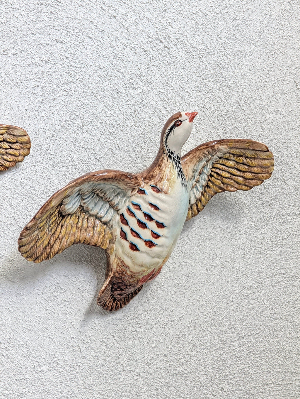 Ceramic quail wall decoration with wings spread mounted on textured white wall