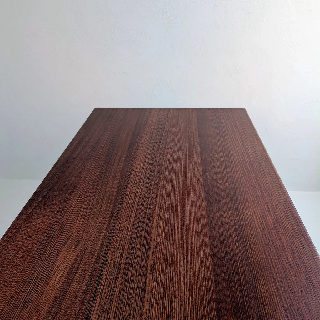 Close-up view of smooth, polished dark wooden table surface against plain light wall