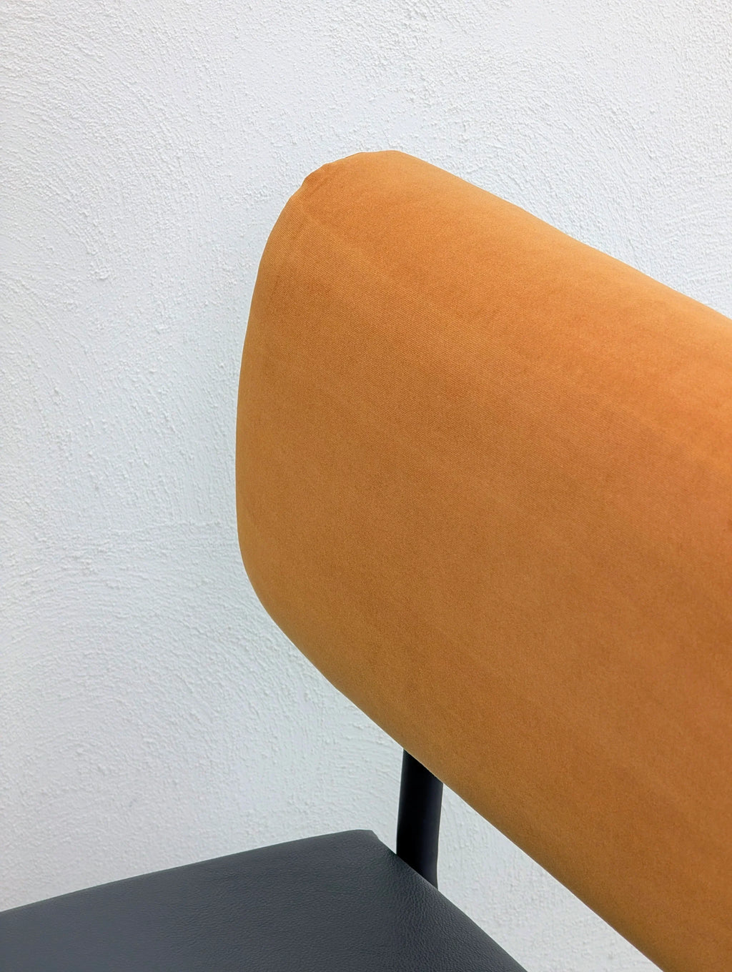 Modern chair with orange fabric backrest and black seat against a white textured wall