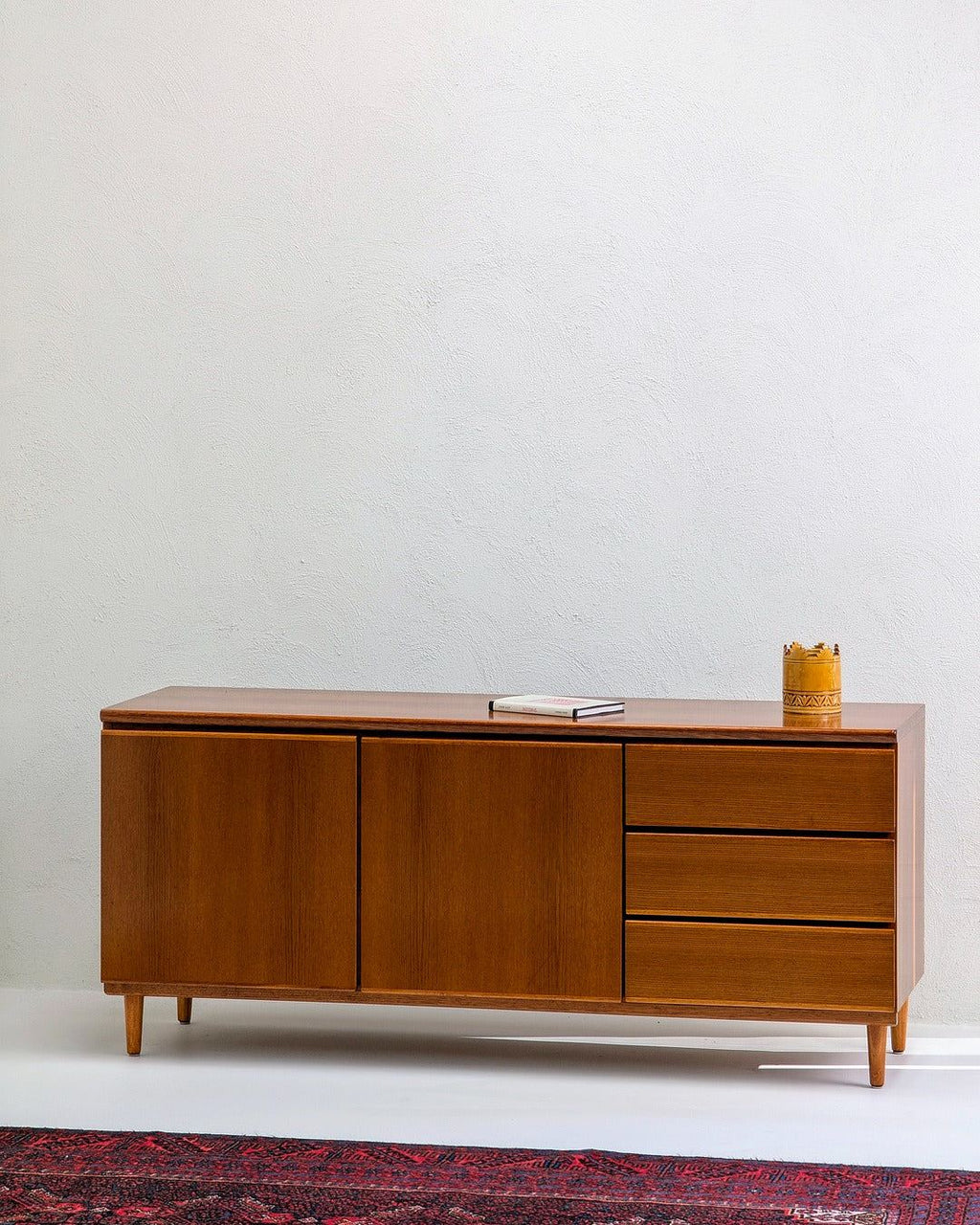 Mid-century modern wooden sideboard with three drawers, book and decor on top, white wall background