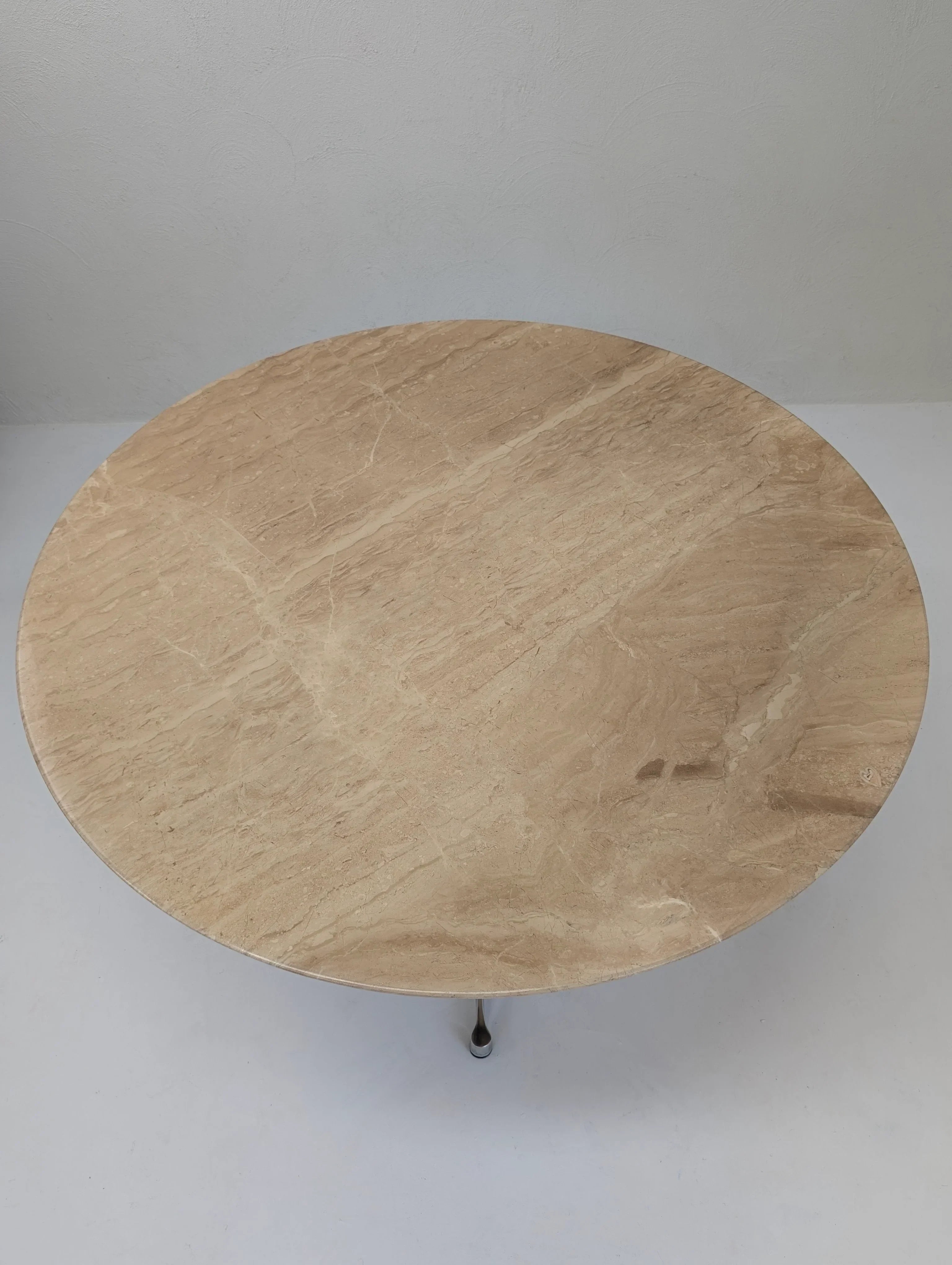 Round beige marble coffee table with thin metal legs on a light floor