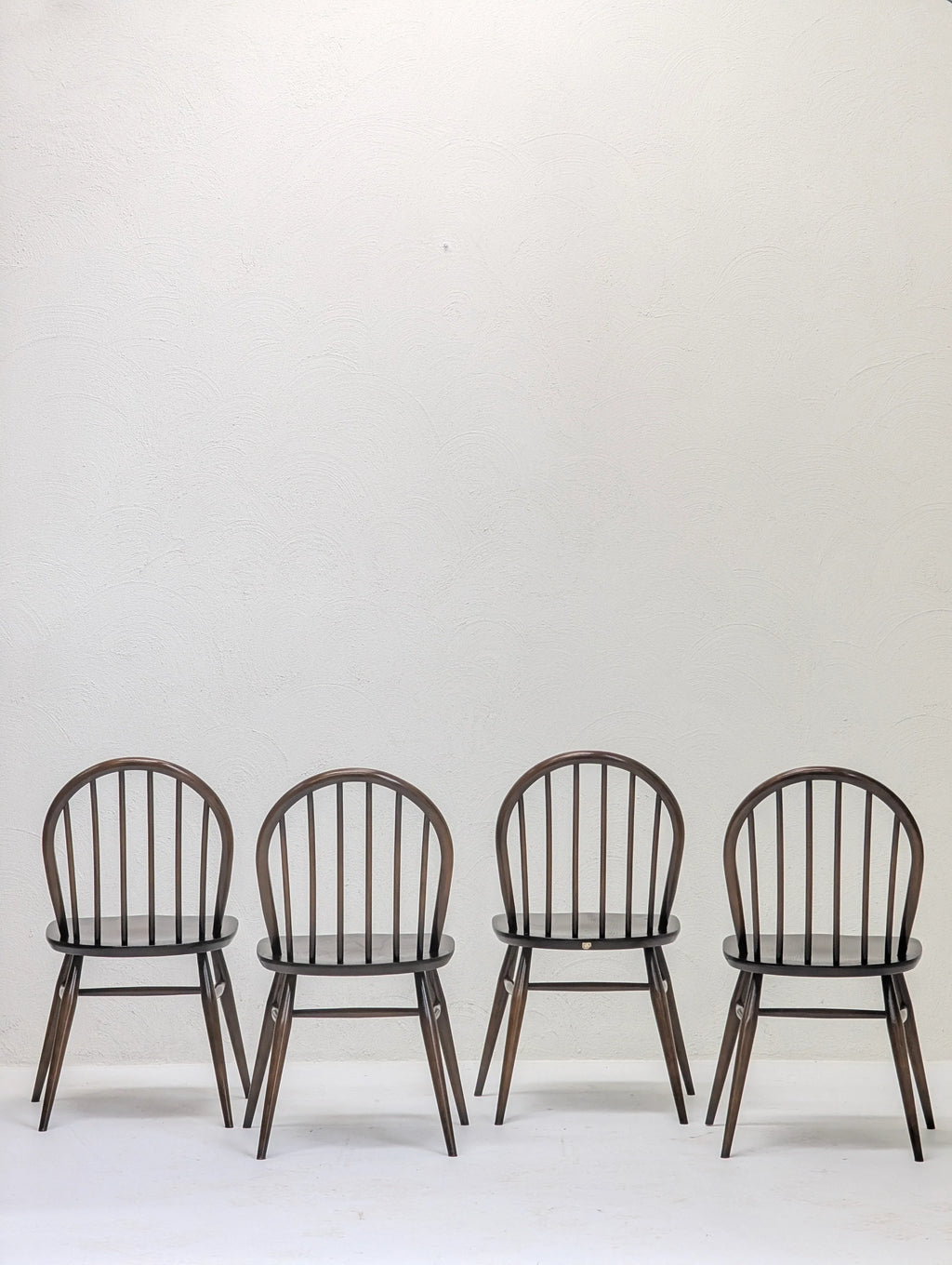 Four dark wooden classic spindle back chairs against a textured white wall