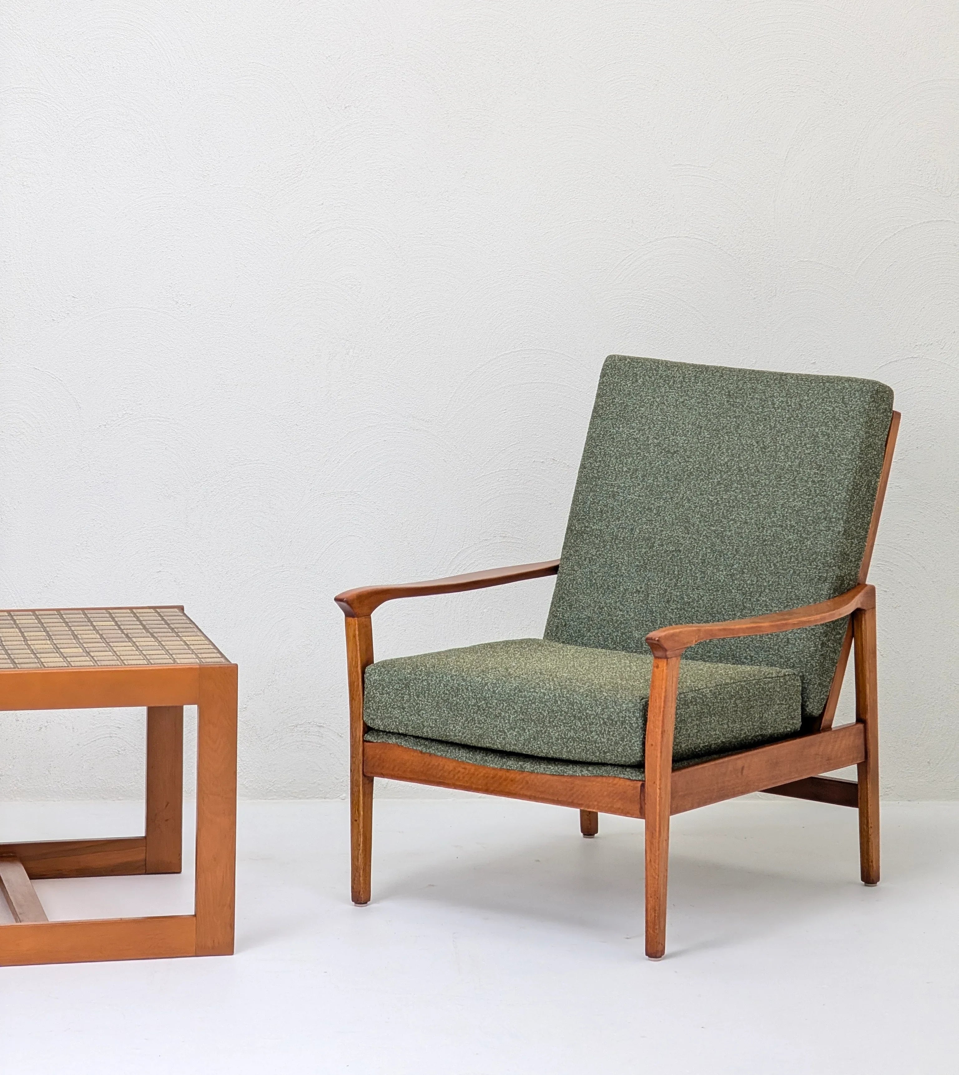 Mid-century modern wooden armchair with green cushions beside a wooden tiled coffee table