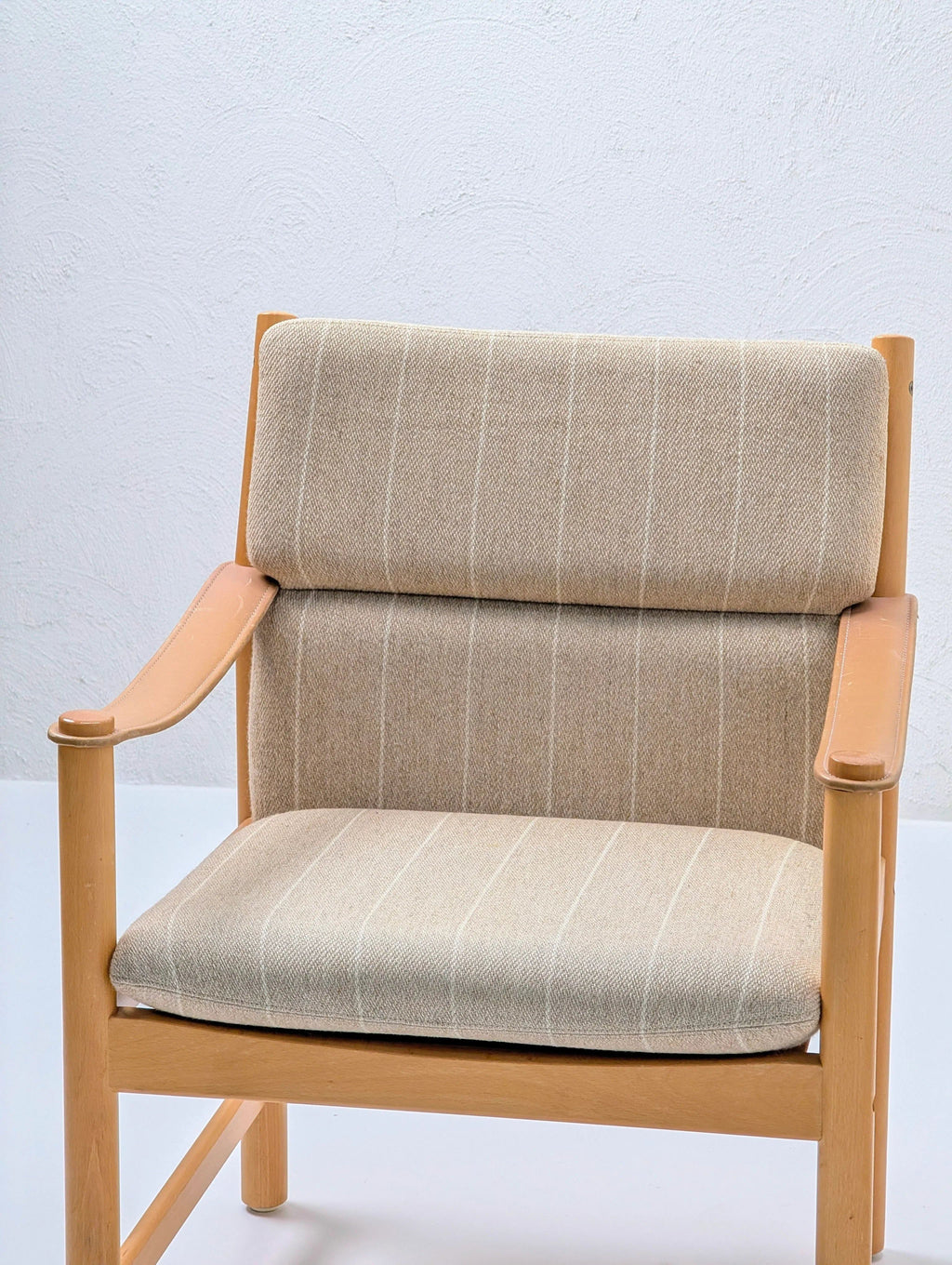 Beige upholstered wooden armchair with vertical stripes in minimalist setting