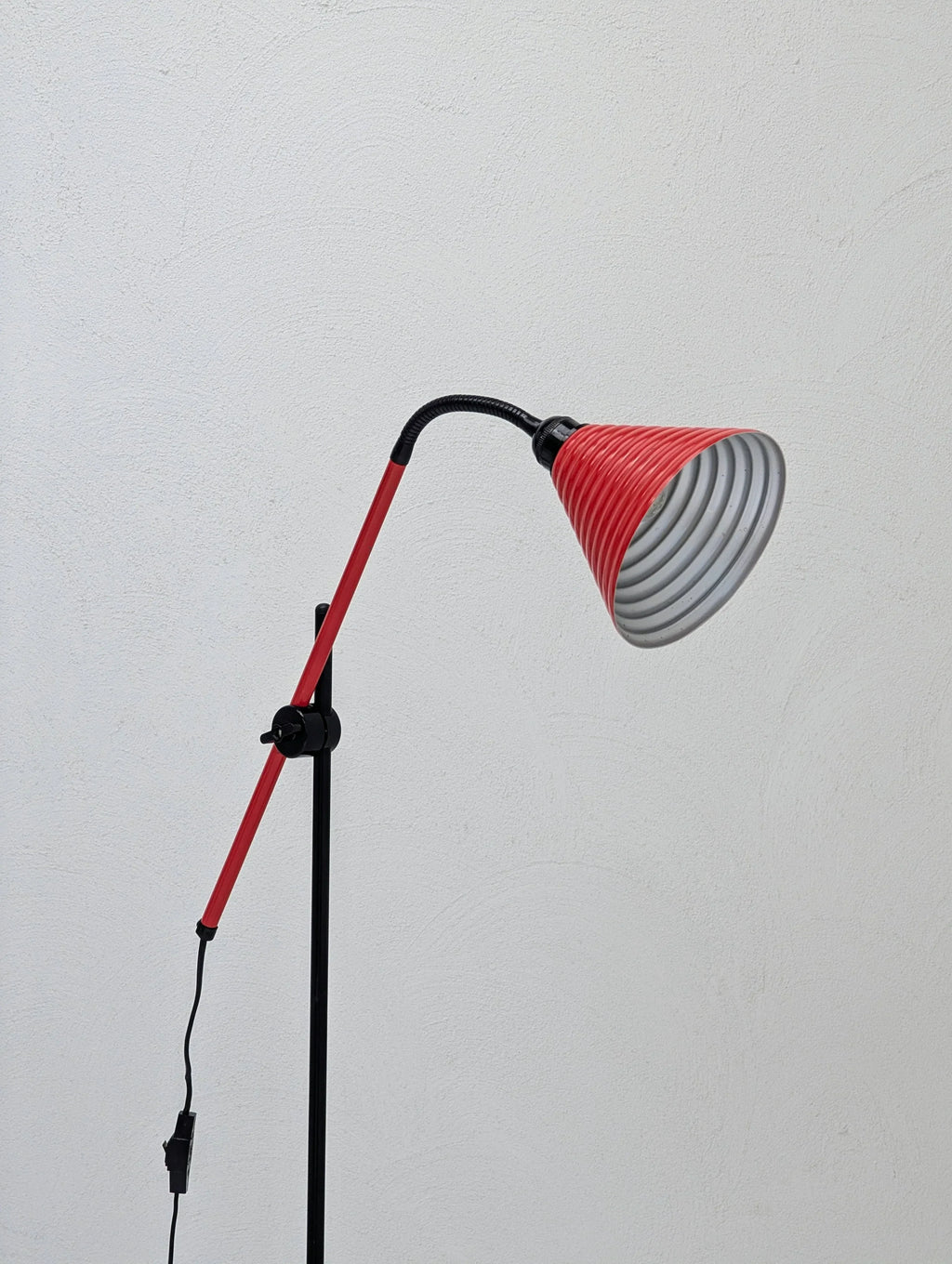 Modern red floor lamp with adjustable arm against a plain white textured wall