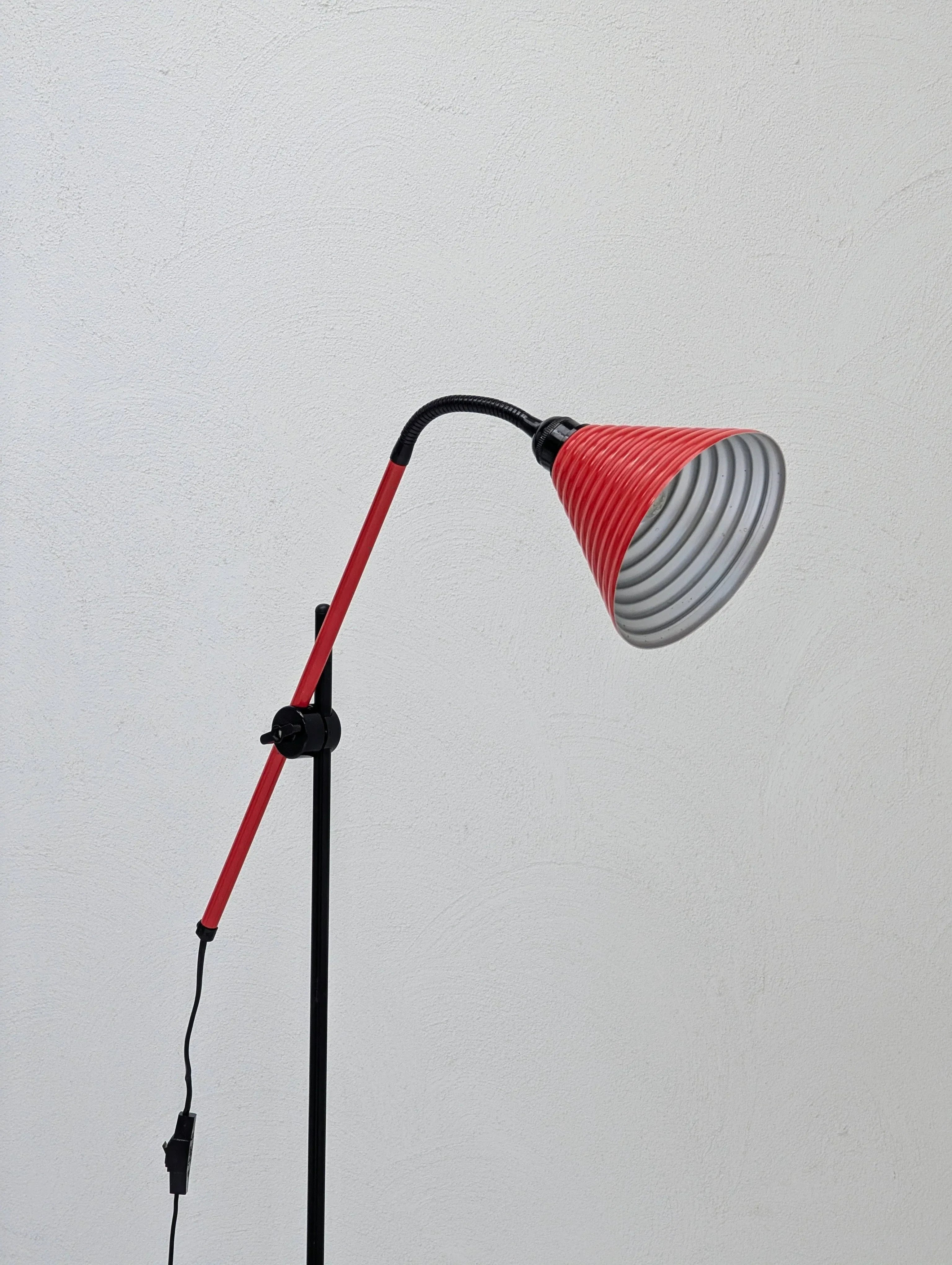 Modern red floor lamp with adjustable arm against a plain white textured wall