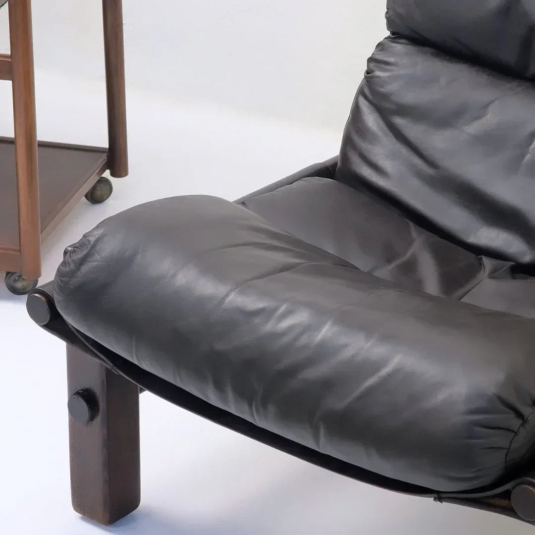 Black leather lounge chair with wooden legs next to a wooden side table on wheels