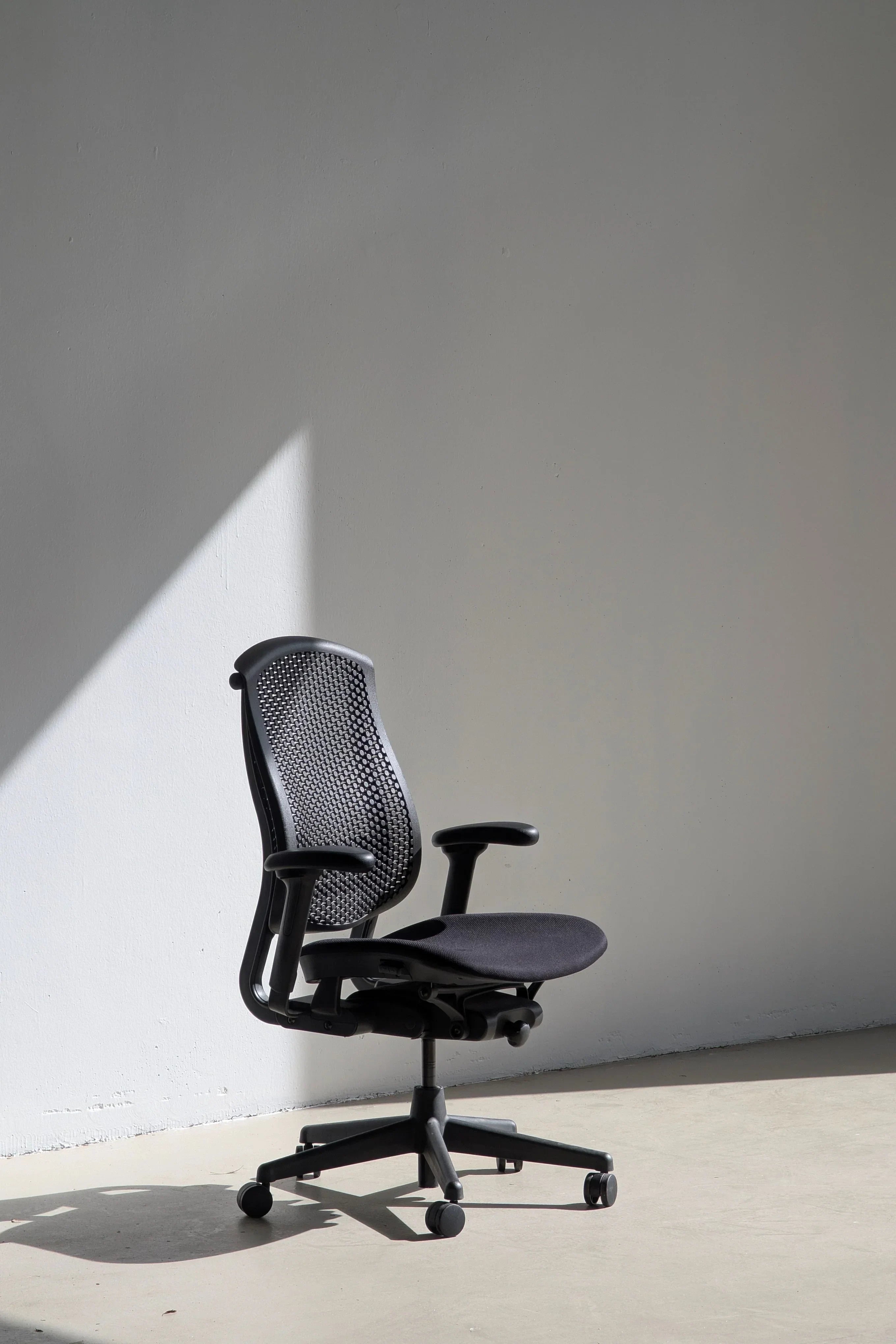 Modern ergonomic black office chair with mesh backrest in sunlight against minimal wall