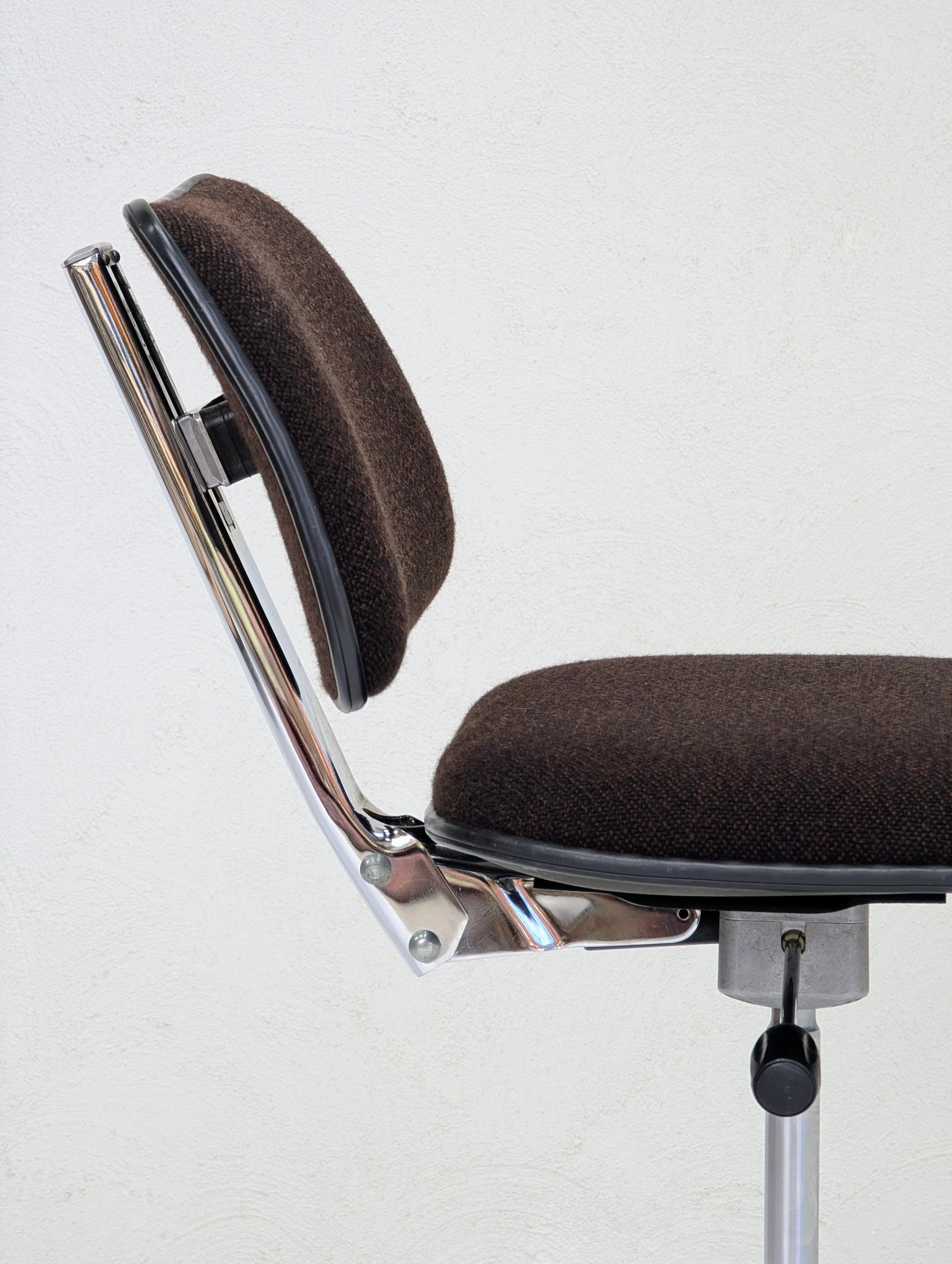 Side view of a brown cushioned office chair with chrome frame against a white wall