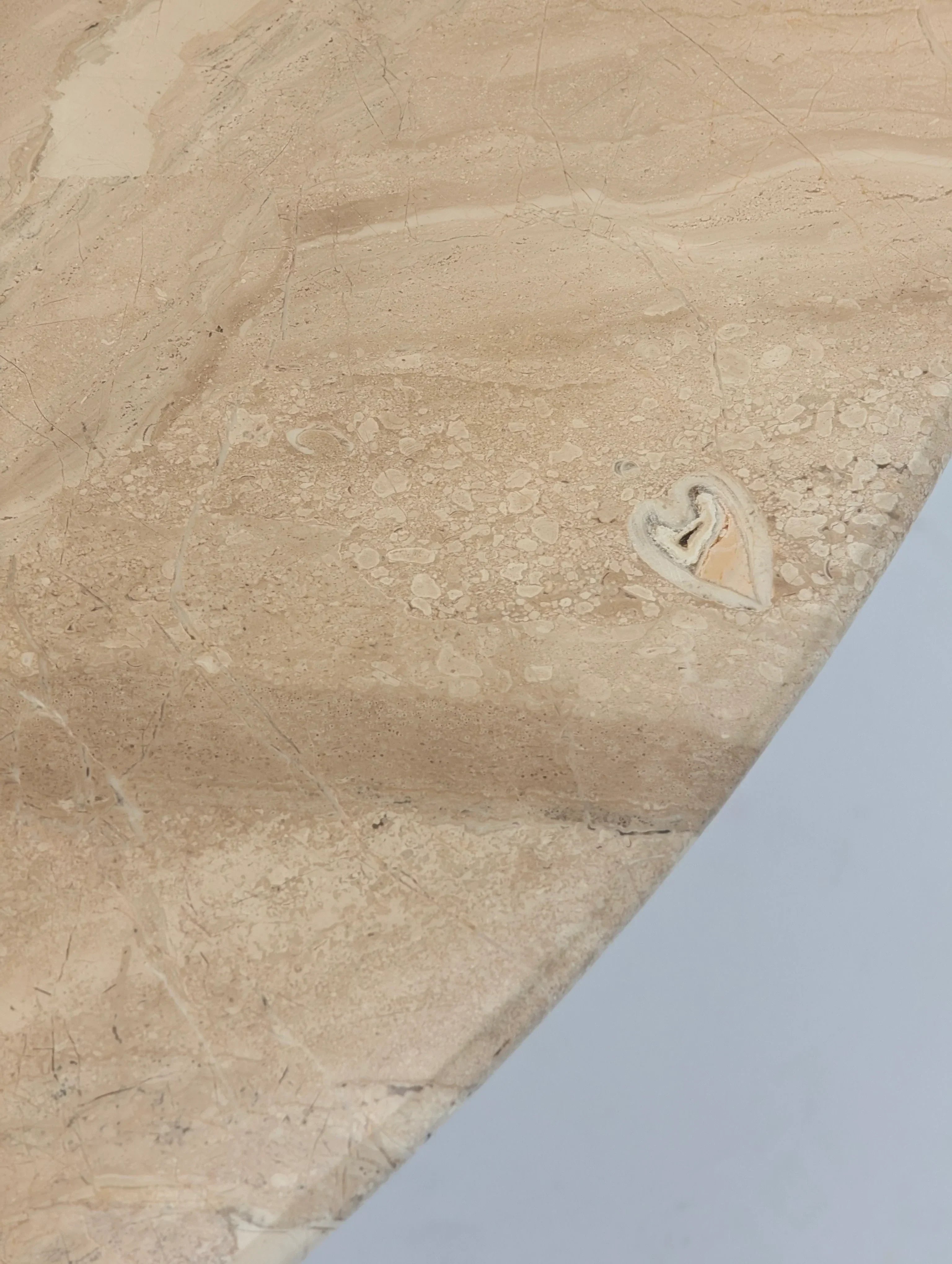 Beige marble tabletop with natural heart-shaped fossil detail and subtle veining