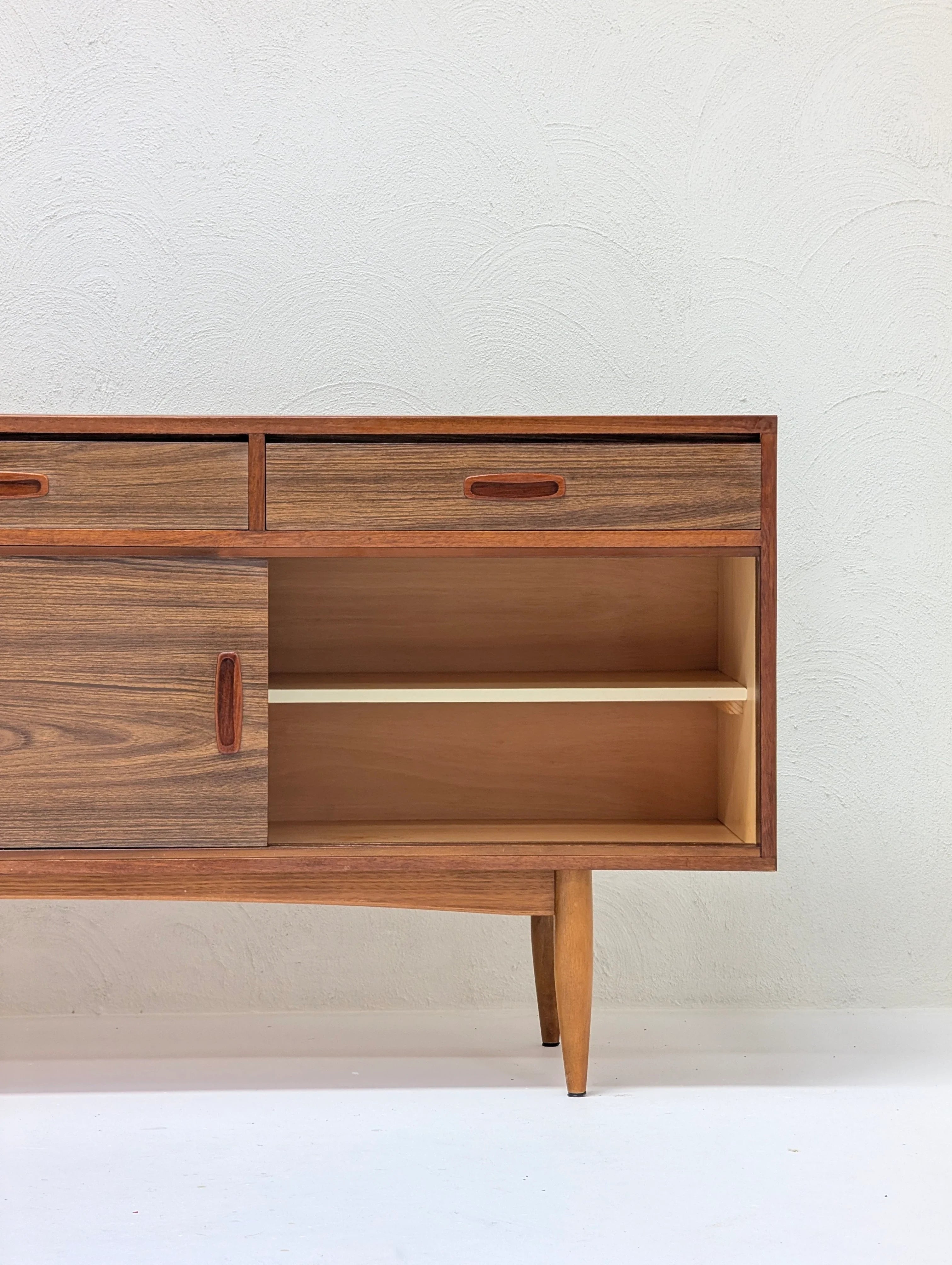 Mid-century modern wooden sideboard with drawers and open shelf against textured white wall