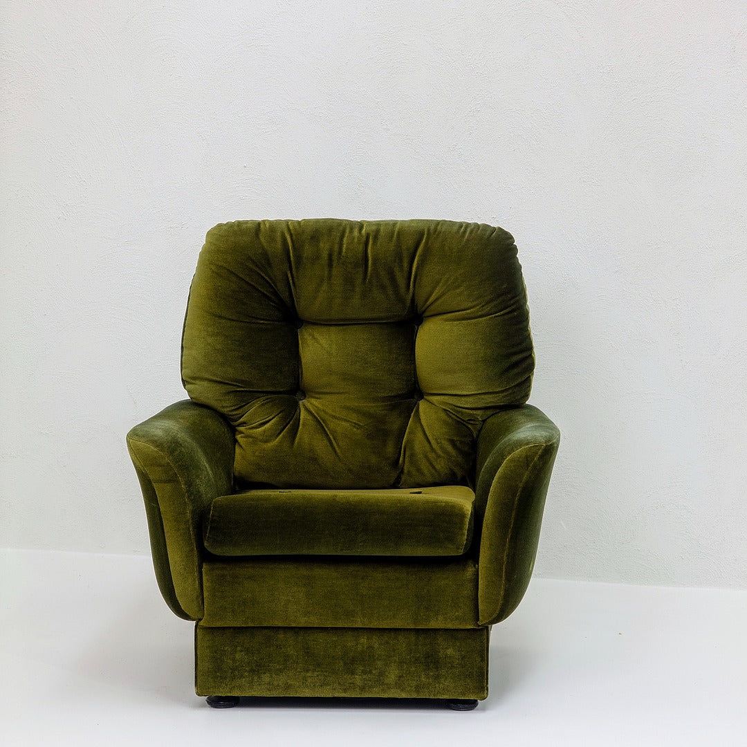 Vintage green velvet armchair against a plain white wall, retro furniture design