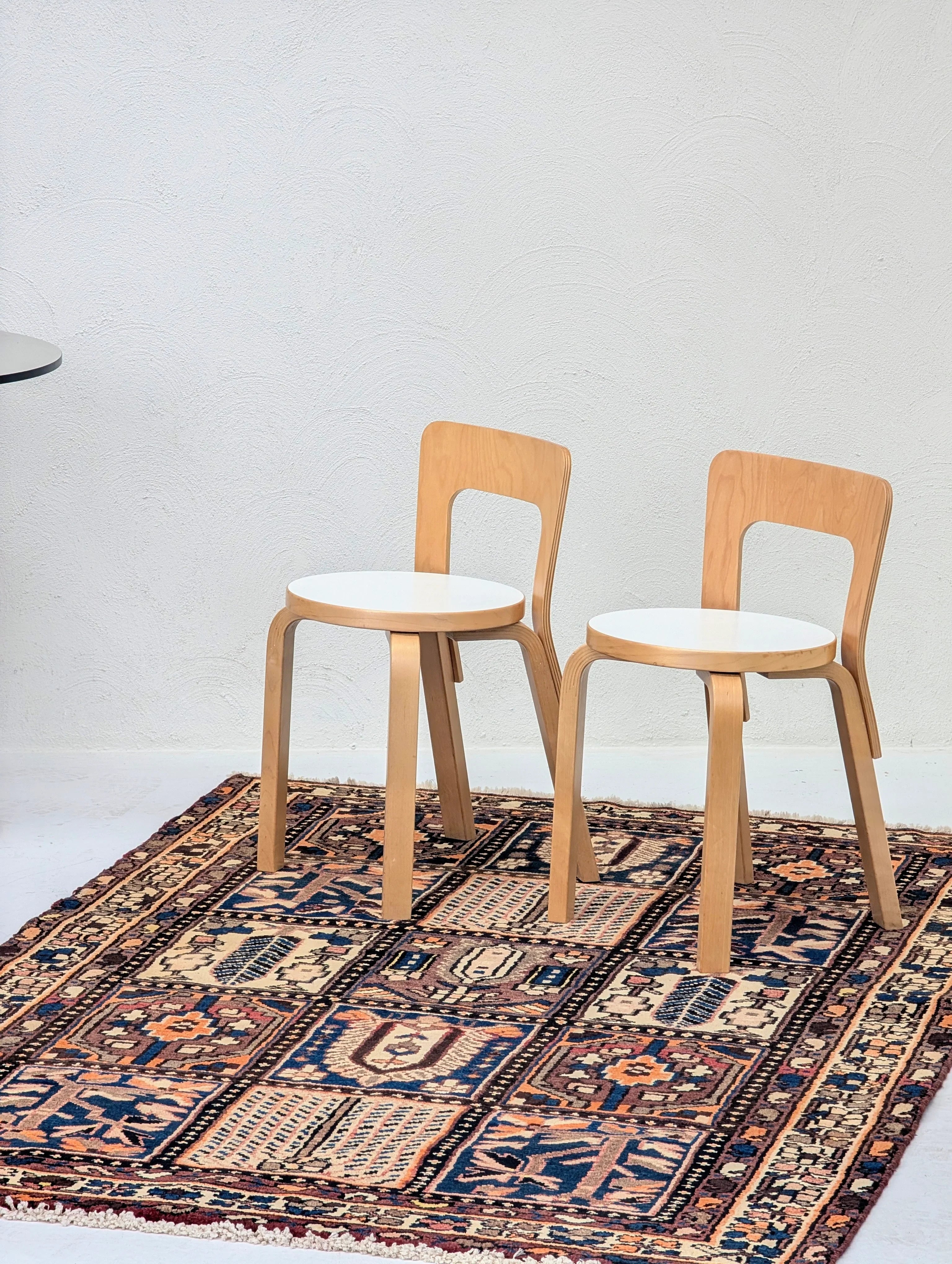 Two wooden chairs with white round seats on a colorful patterned rug against a white textured wall