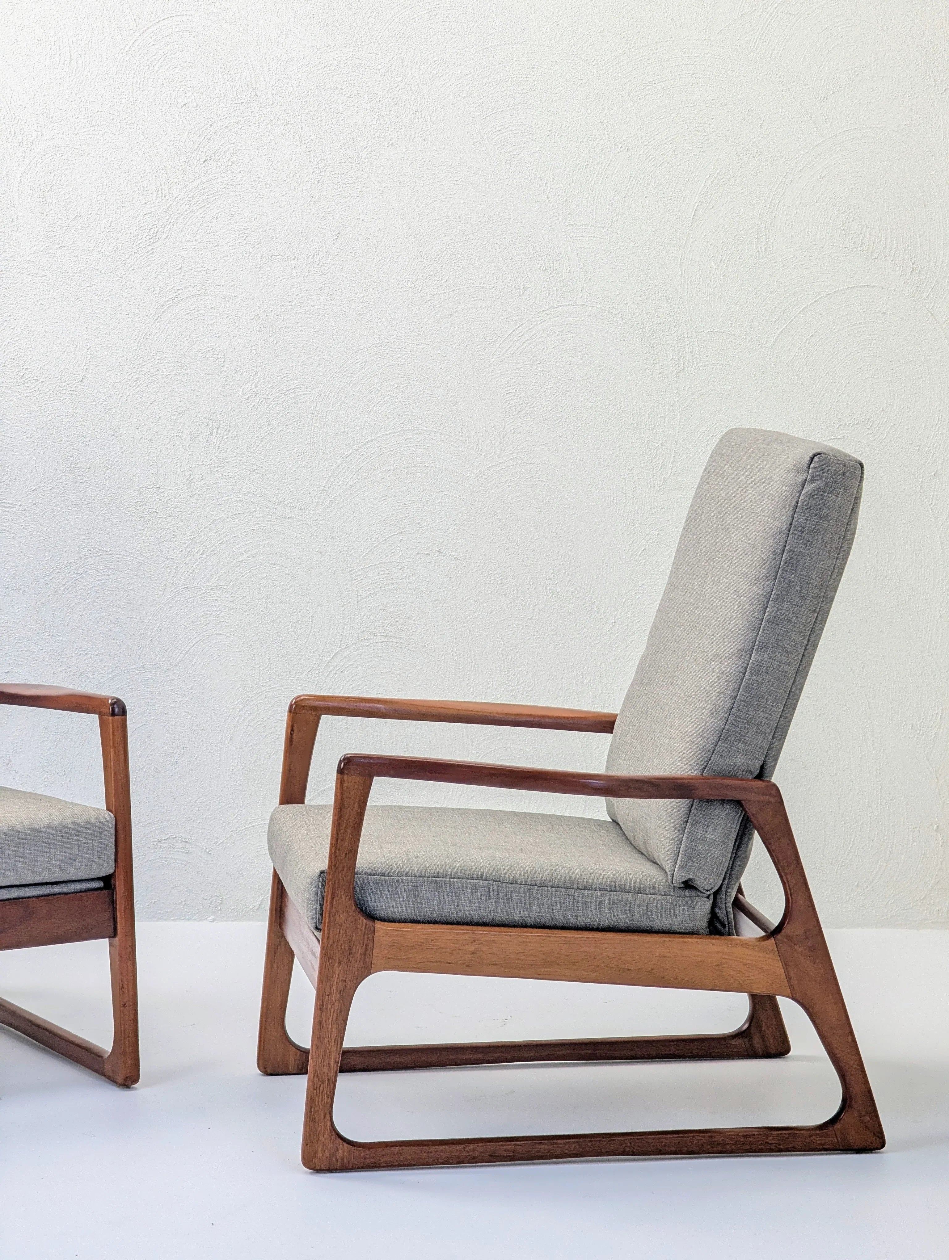 Mid-century modern wooden armchair with grey cushion against a white textured wall