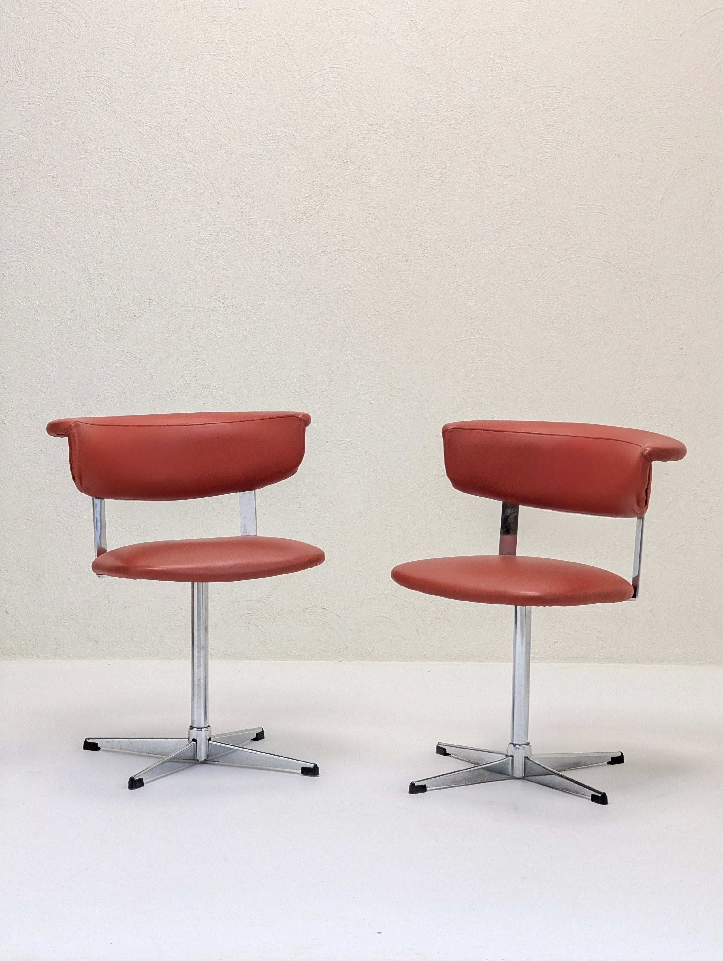 Pair of vintage brown leather swivel chairs with chrome metal bases on white floor