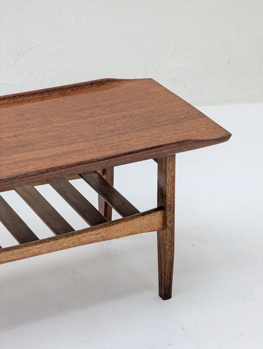Mid-century modern wooden coffee table with slatted lower shelf on white backdrop