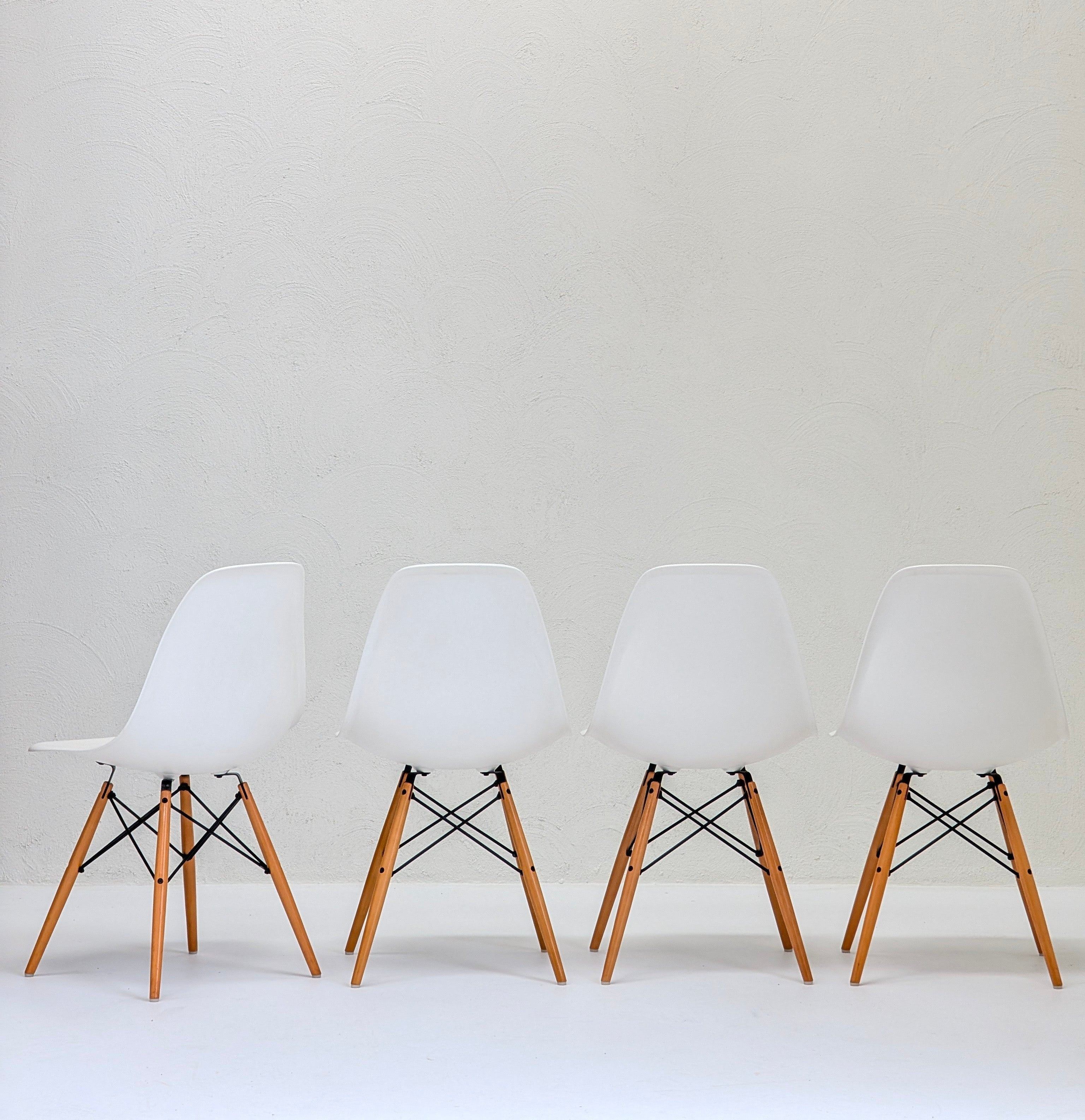 Four modern white chairs with wooden legs lined up against a textured white wall