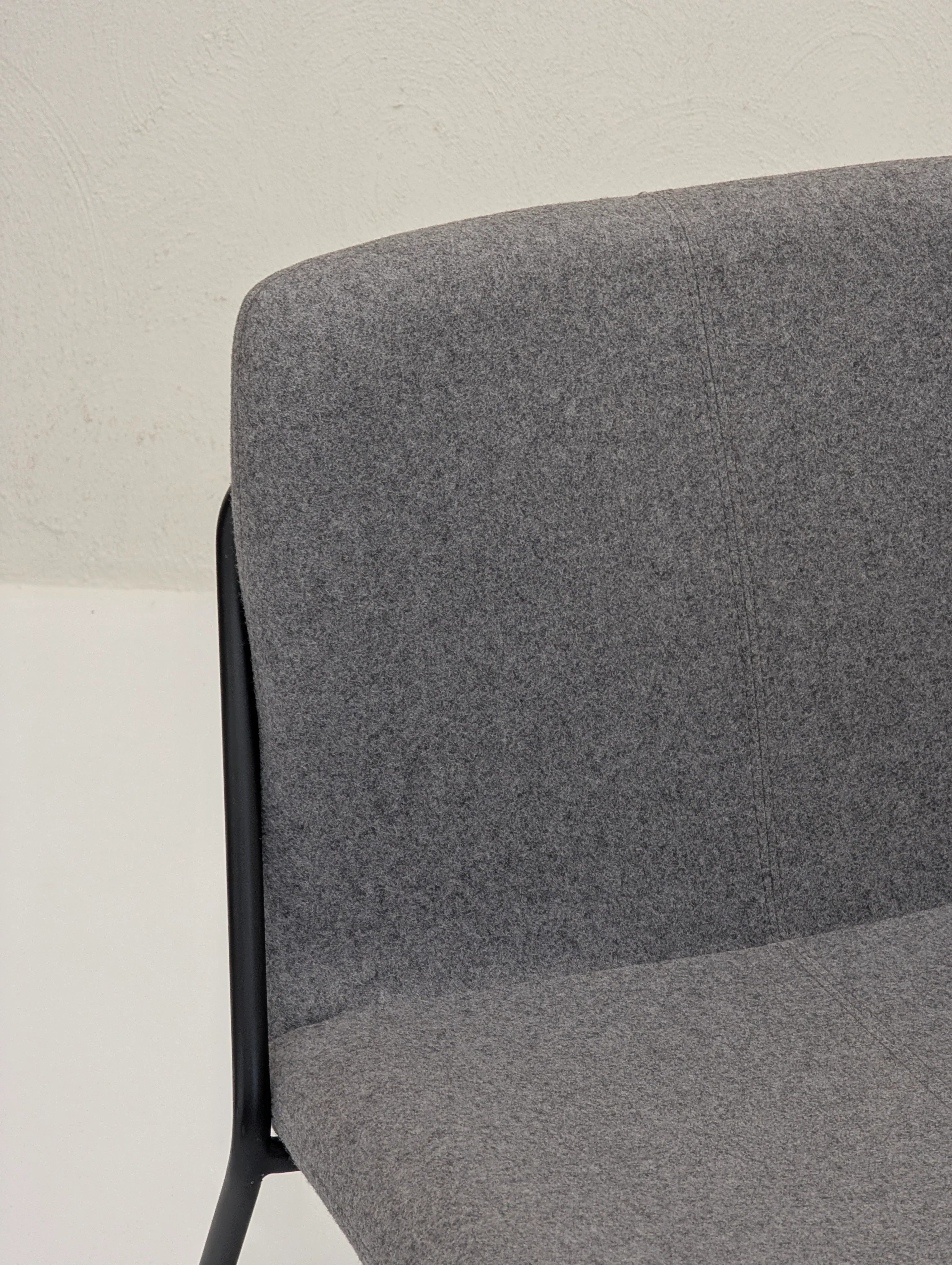 Modern gray fabric upholstered chair with black metal frame against beige wall