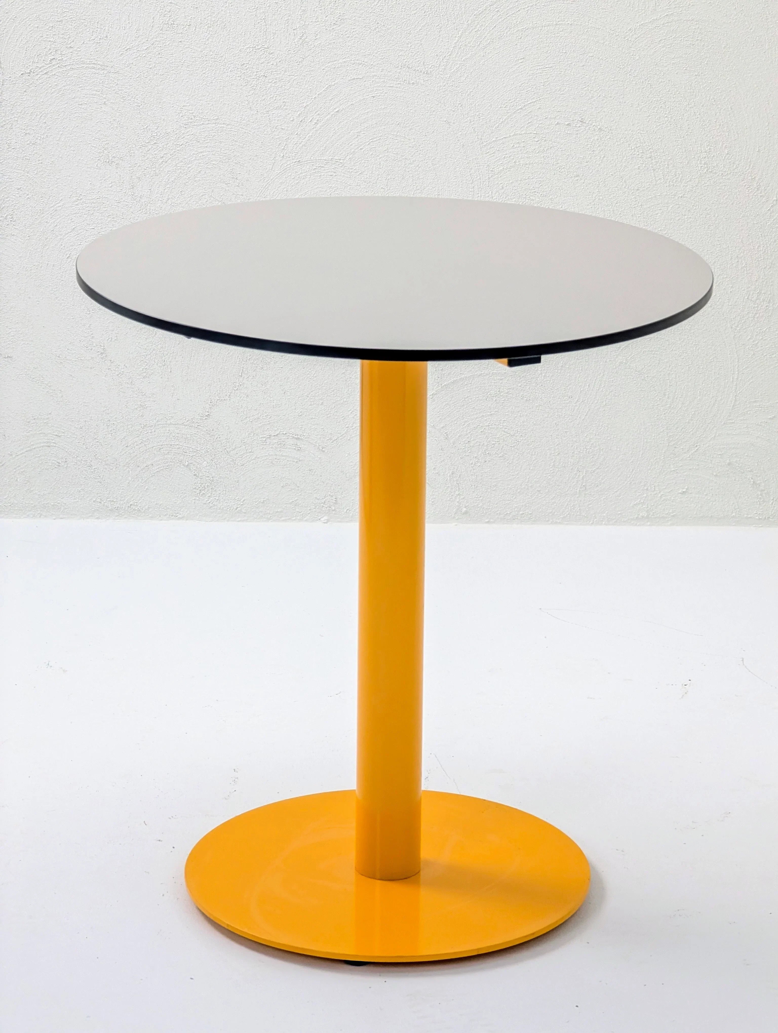 Modern round table with yellow metal base and light gray top against white wall