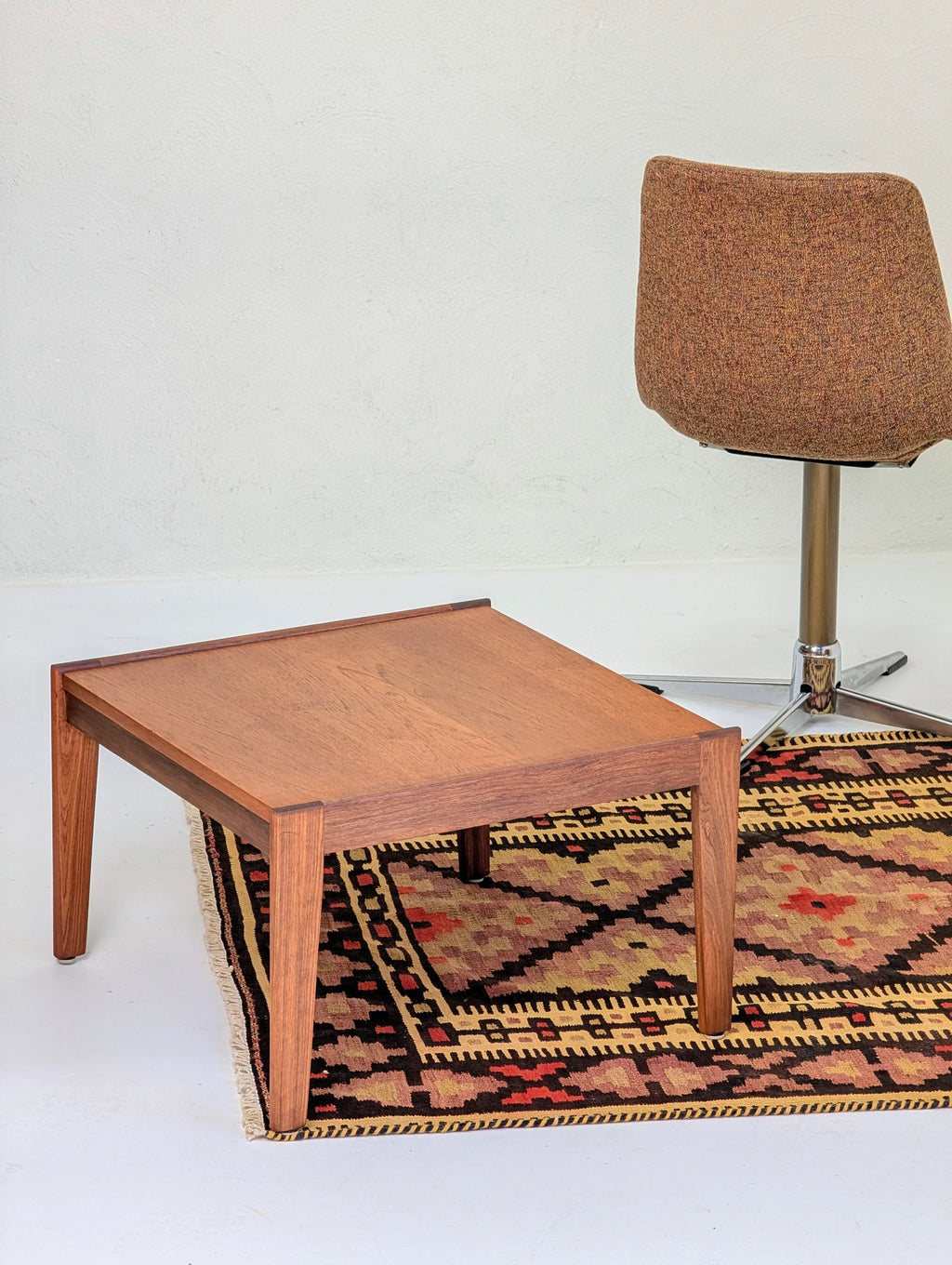 wooden square coffee table on patterned area rug beside brown swivel chair in minimalist room