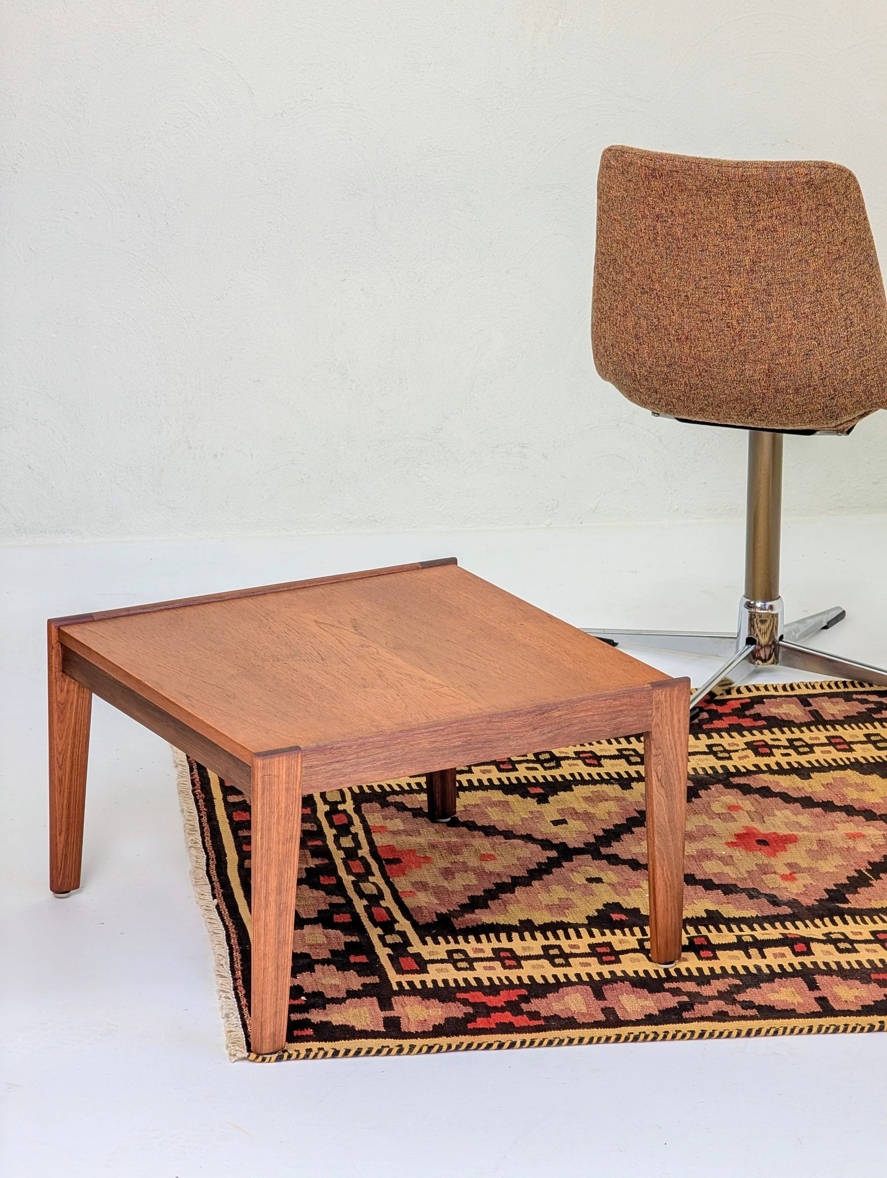 wooden square coffee table on patterned area rug beside brown swivel chair in minimalist room