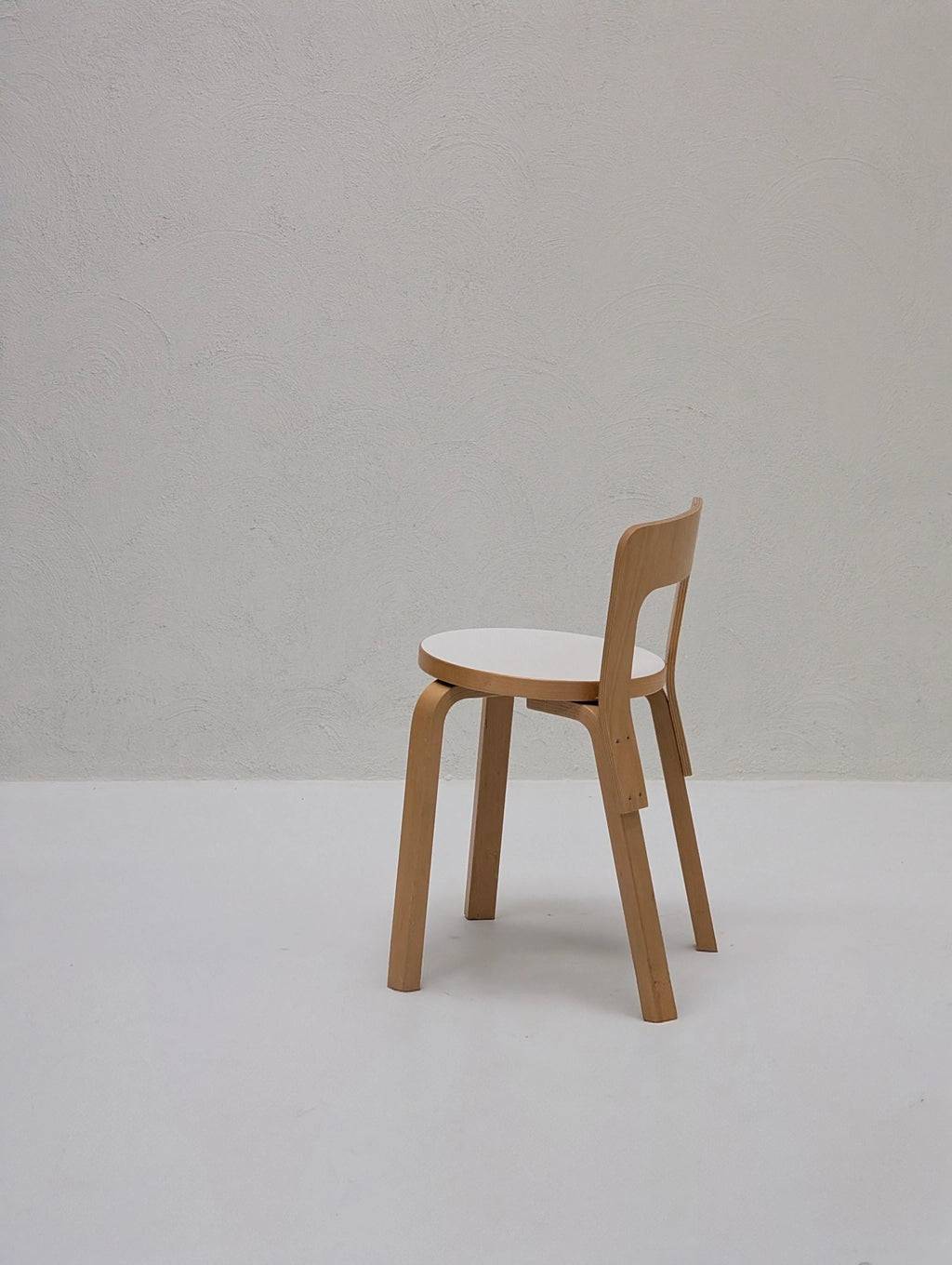 Minimalist wooden chair with white seat in empty room with textured white wall