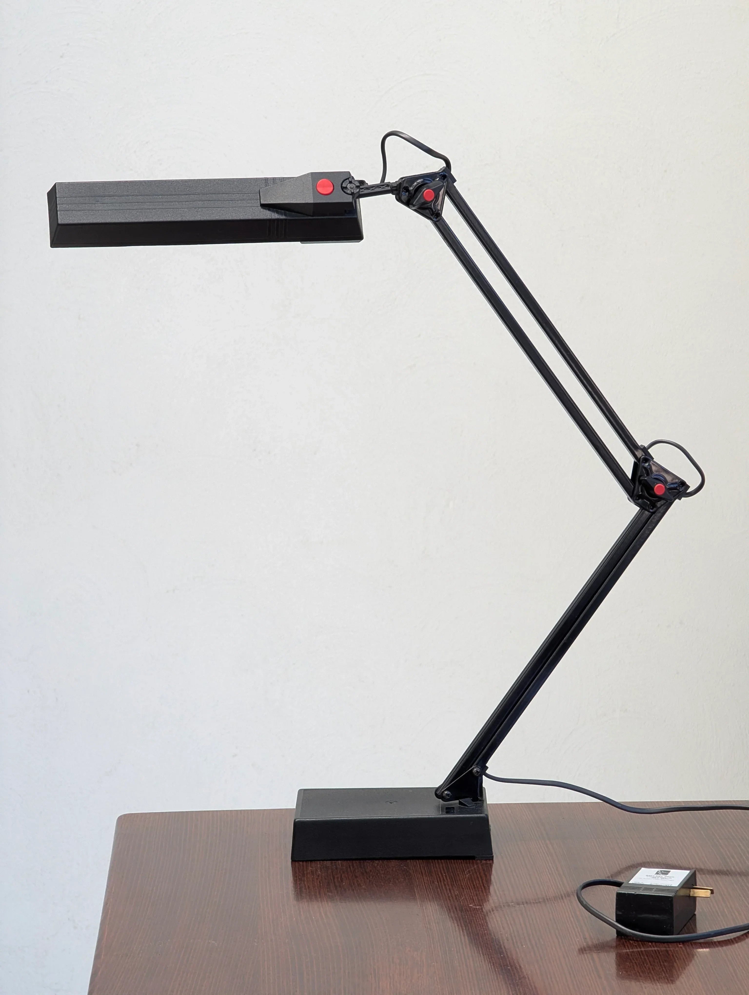 Black adjustable desk lamp with red accents on a wooden table, modern workspace lighting