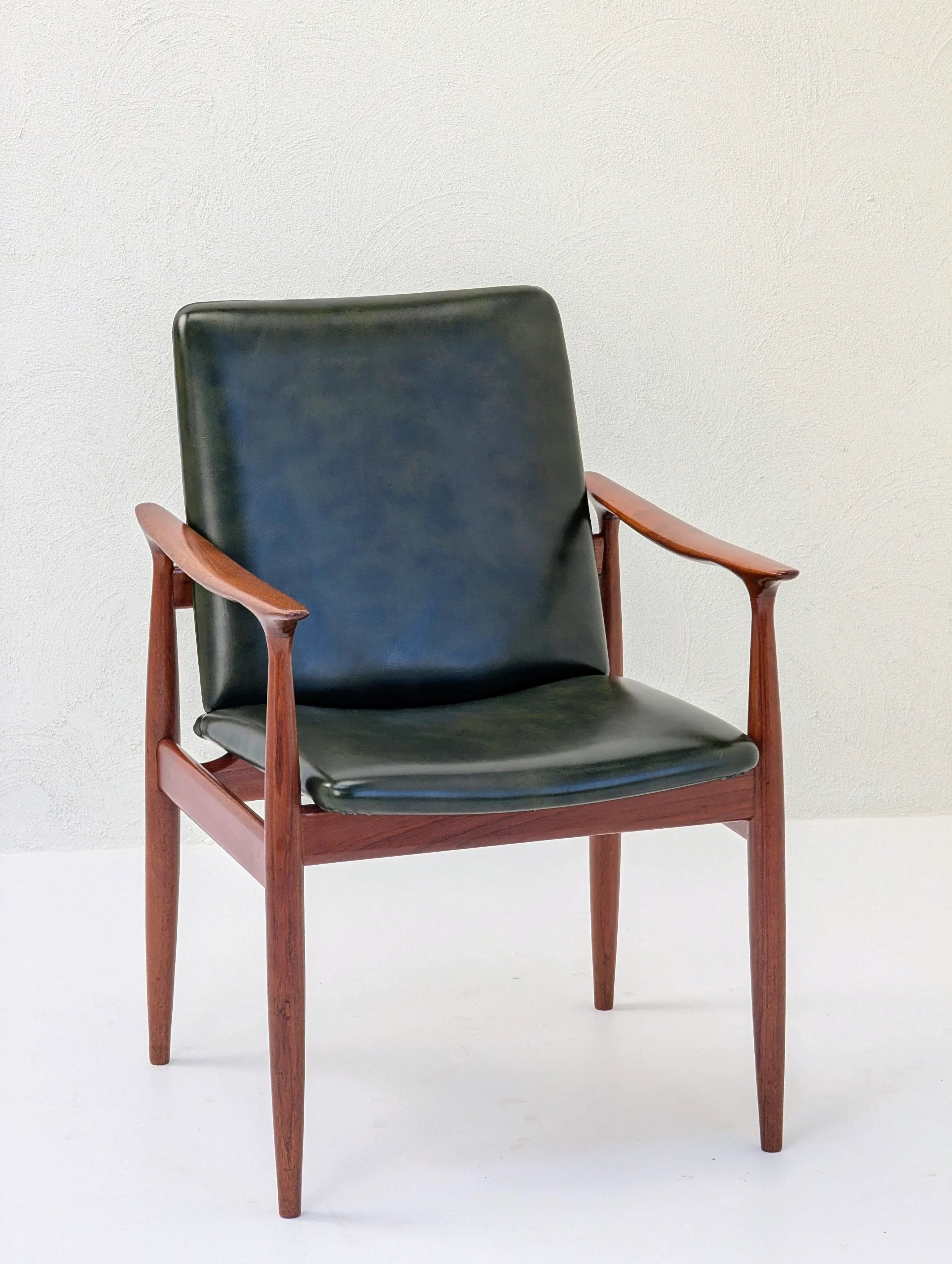 Mid-century modern wooden armchair with dark green leather seat and backrest on white background