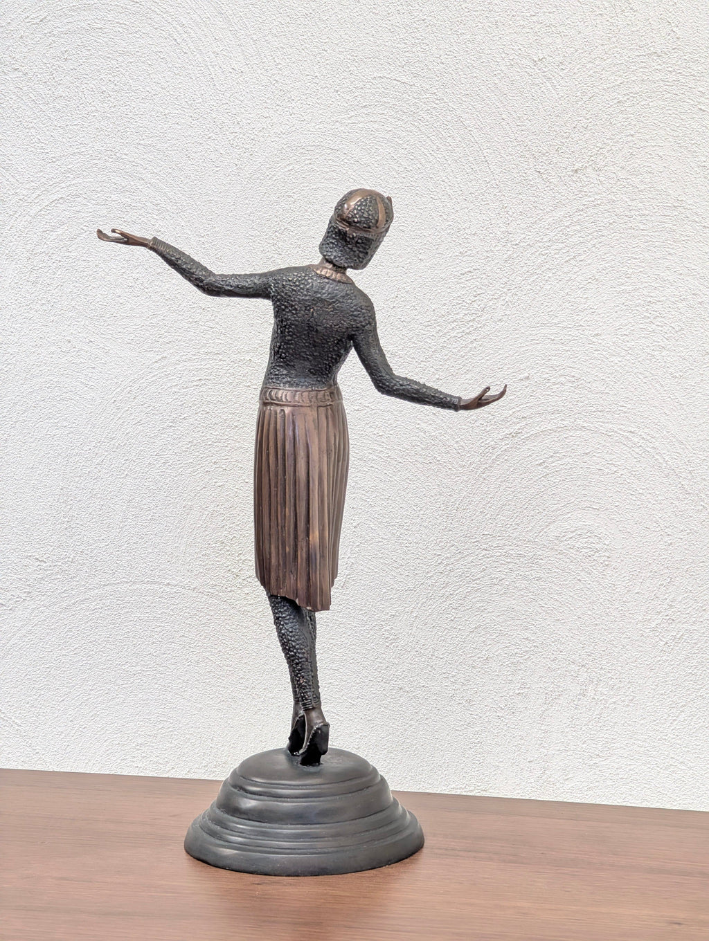 Bronze sculpture of a dancing woman in a textured dress and hat on a black round base