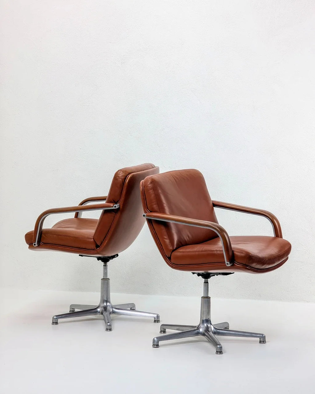 Pair of vintage brown leather office chairs with chrome bases on white background