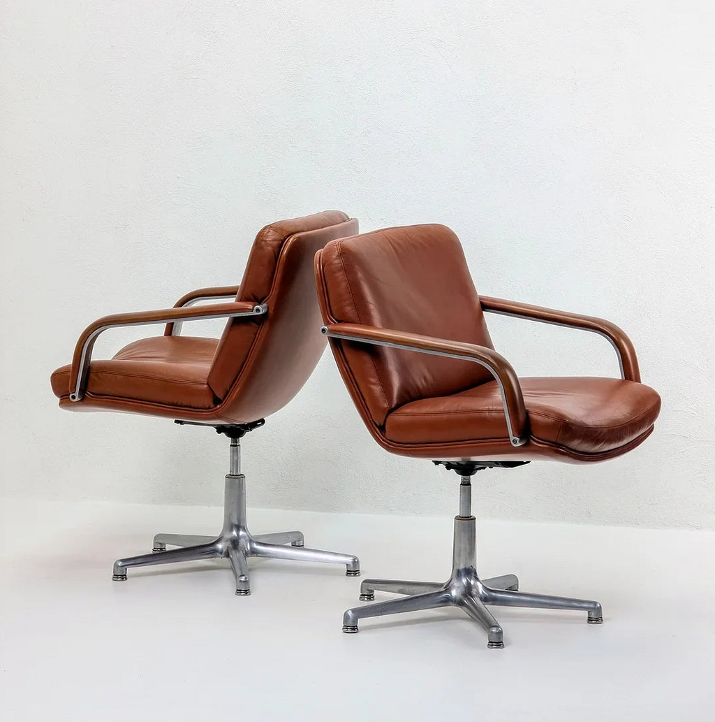 Pair of mid-century modern brown leather swivel office chairs with metal bases on white floor