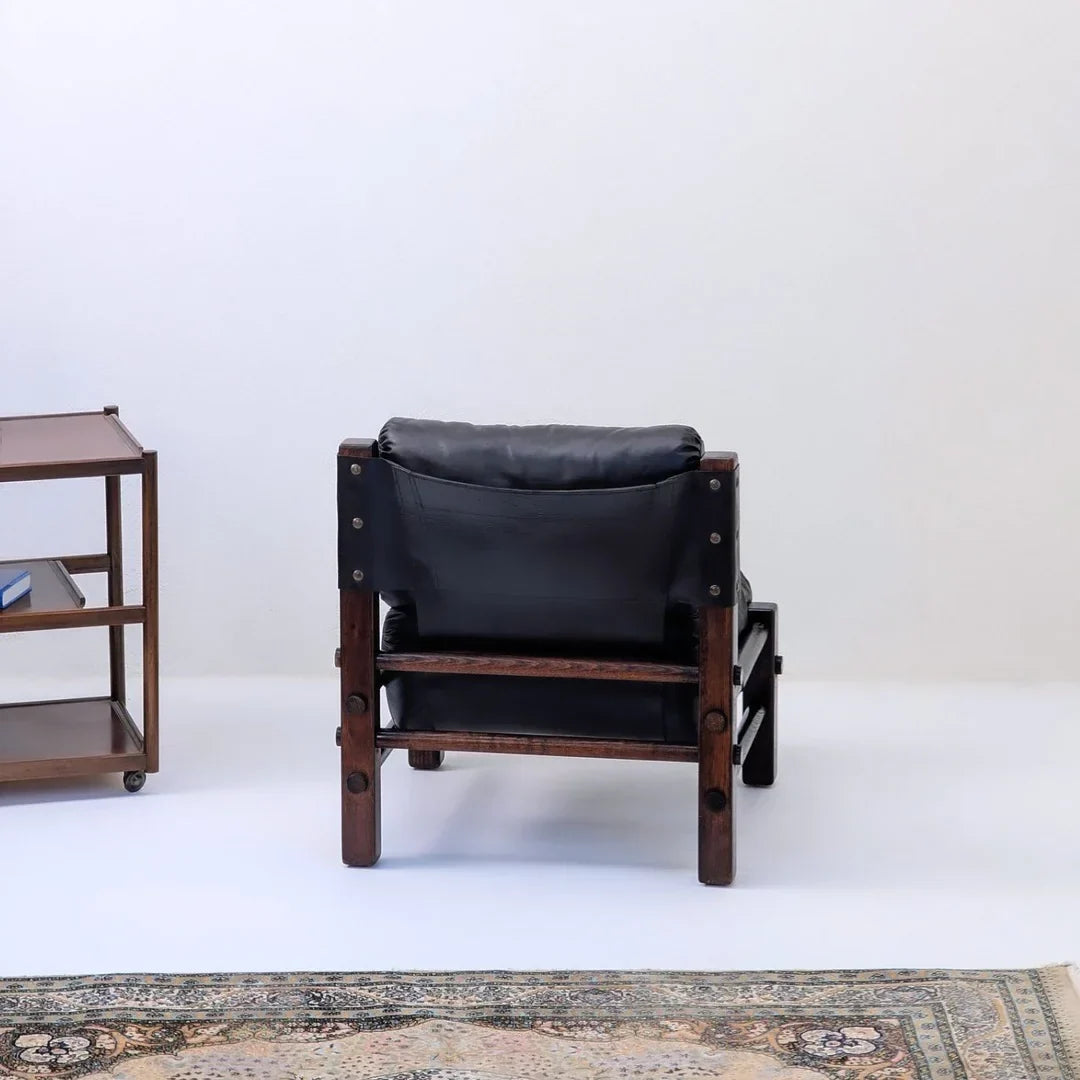Mid-century modern black leather armchair with wood frame, vintage rug, and bookshelf