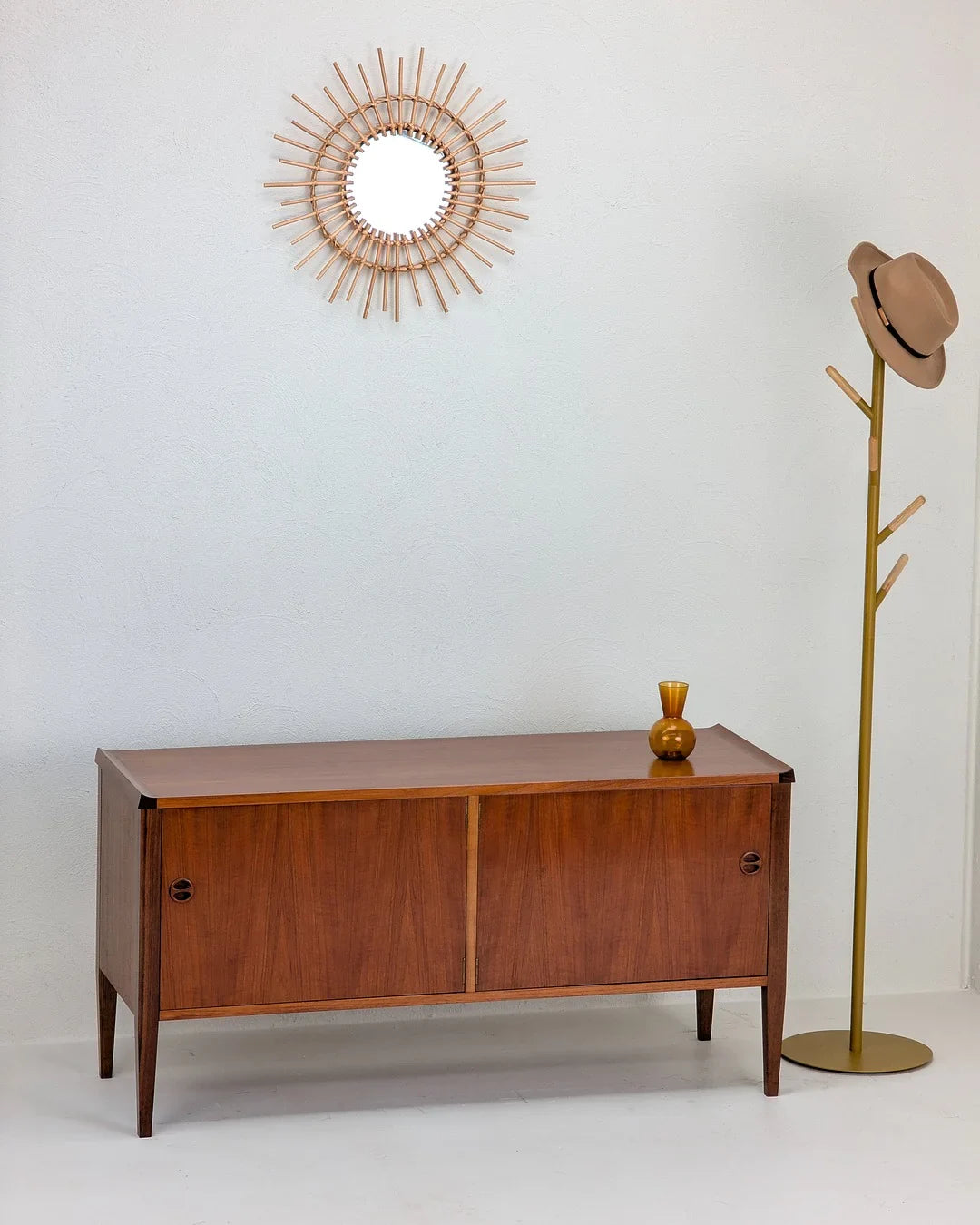 Mid-century modern wooden sideboard, sunburst mirror, gold coat rack with hat, minimalist decor